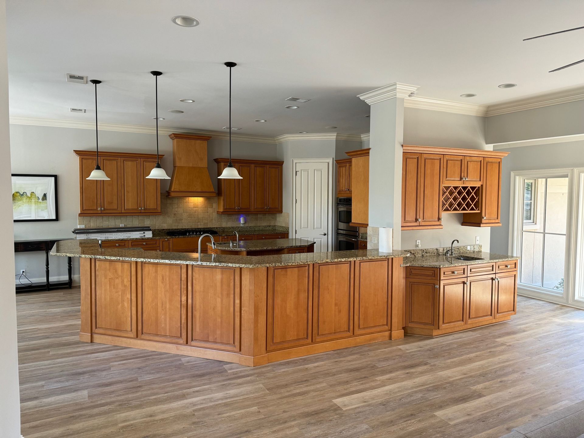 Spacious kitchen with wood cabinets, large island, granite countertops, and light wood flooring.