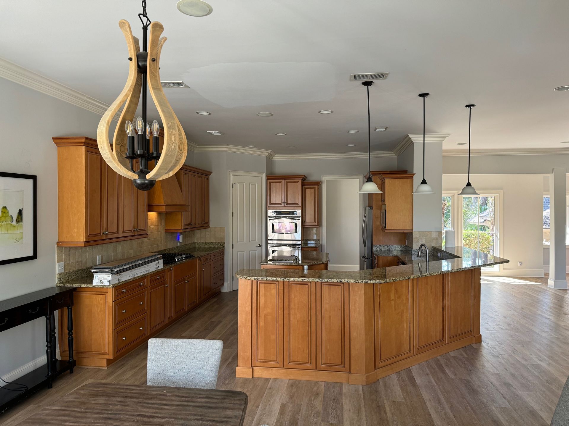 A kitchen with wooden cabinets and island, granite countertops, and pendant lights.