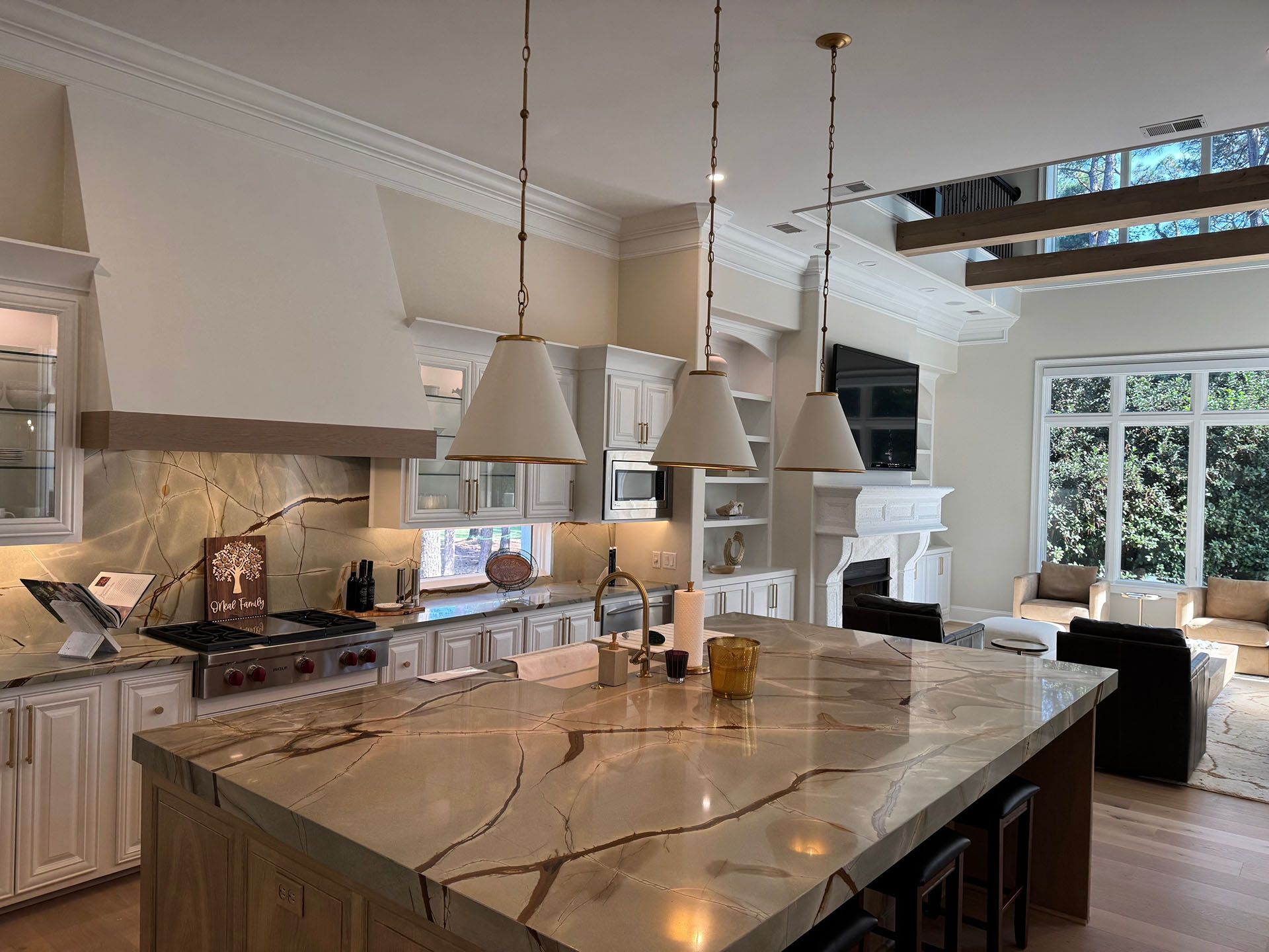 Wexford Home Remodel - After: Kitchen with large island, pendant lights, white cabinetry, and a view of a living area with large windows.