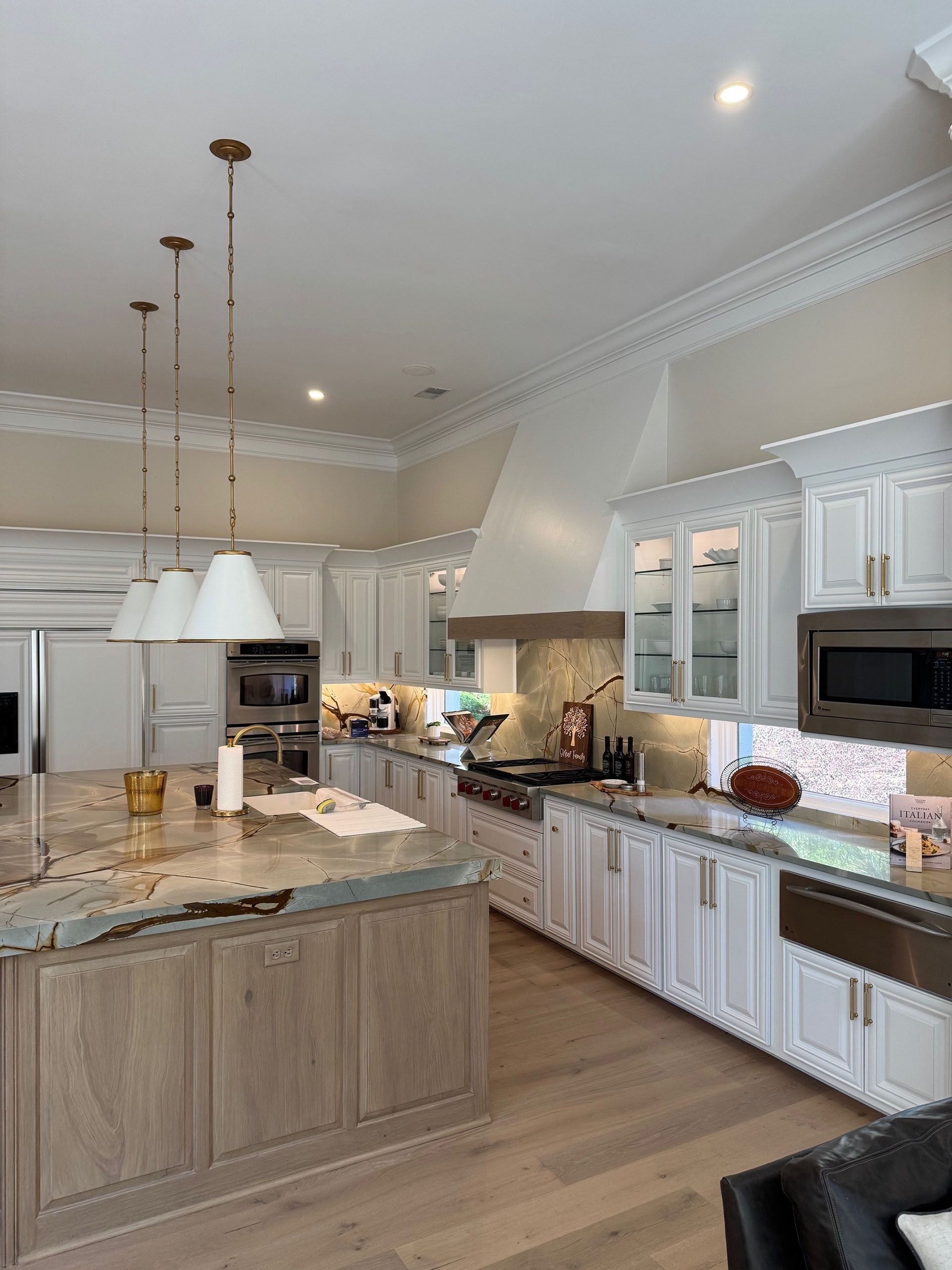 Wexford Home Remodel - After: Spacious white kitchen with island, pendant lights, and stainless steel appliances.