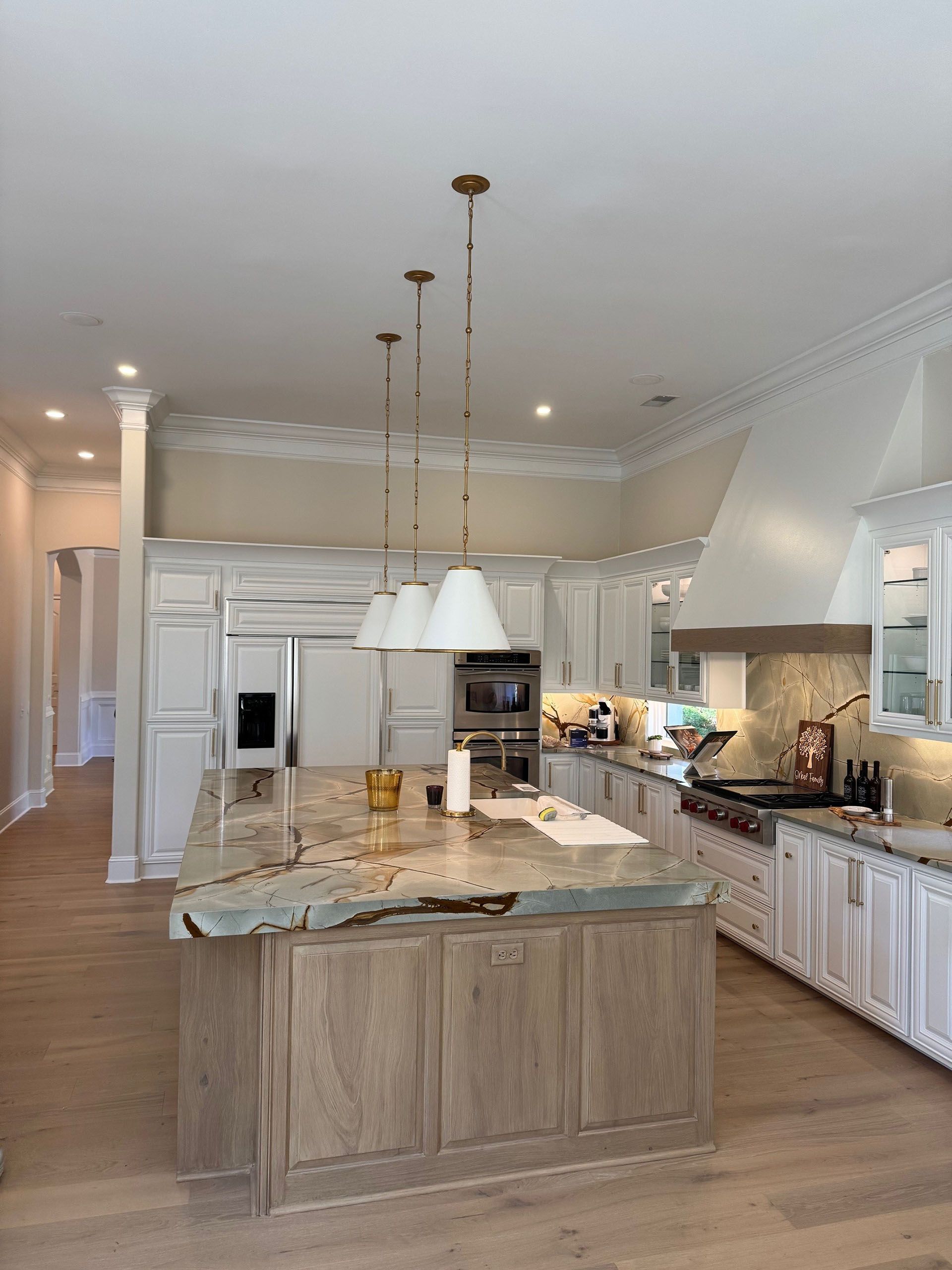 Wexford Home Remodel - After: Large white kitchen with light wood island, gold pendant lights, and stainless steel appliances.