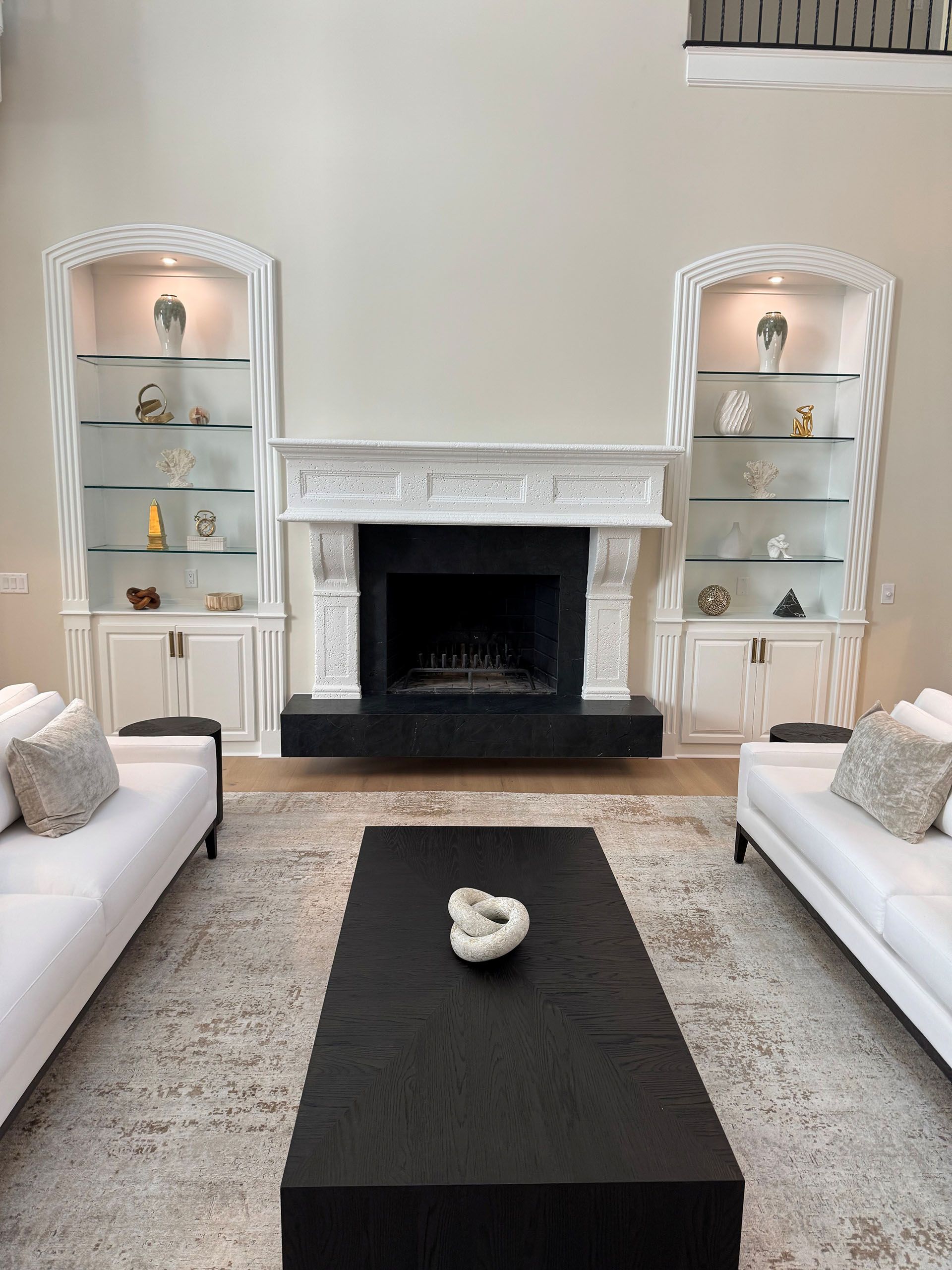 Wexford Home Remodel - After: Living room with fireplace flanked by white bookshelves, two white sofas face each other over a black coffee table.