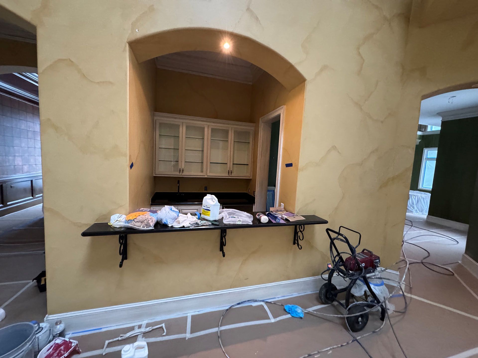 Wexford Home Remodel - Before: Interior with arched opening, built-in cabinets, and a black countertop; painting in progress, yellow walls.