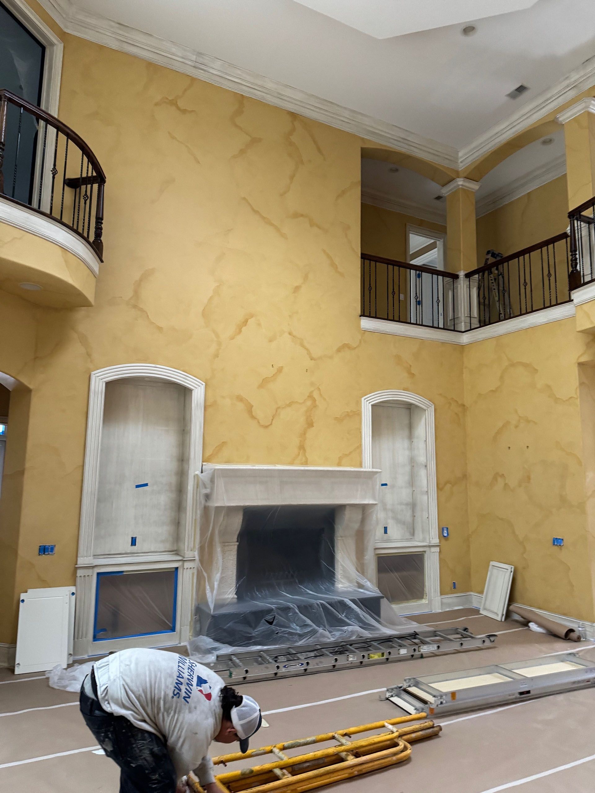 Wexford Home Remodel - Before: Person working on a two-story interior wall painted yellow with faux finish, fireplace, and balconies.