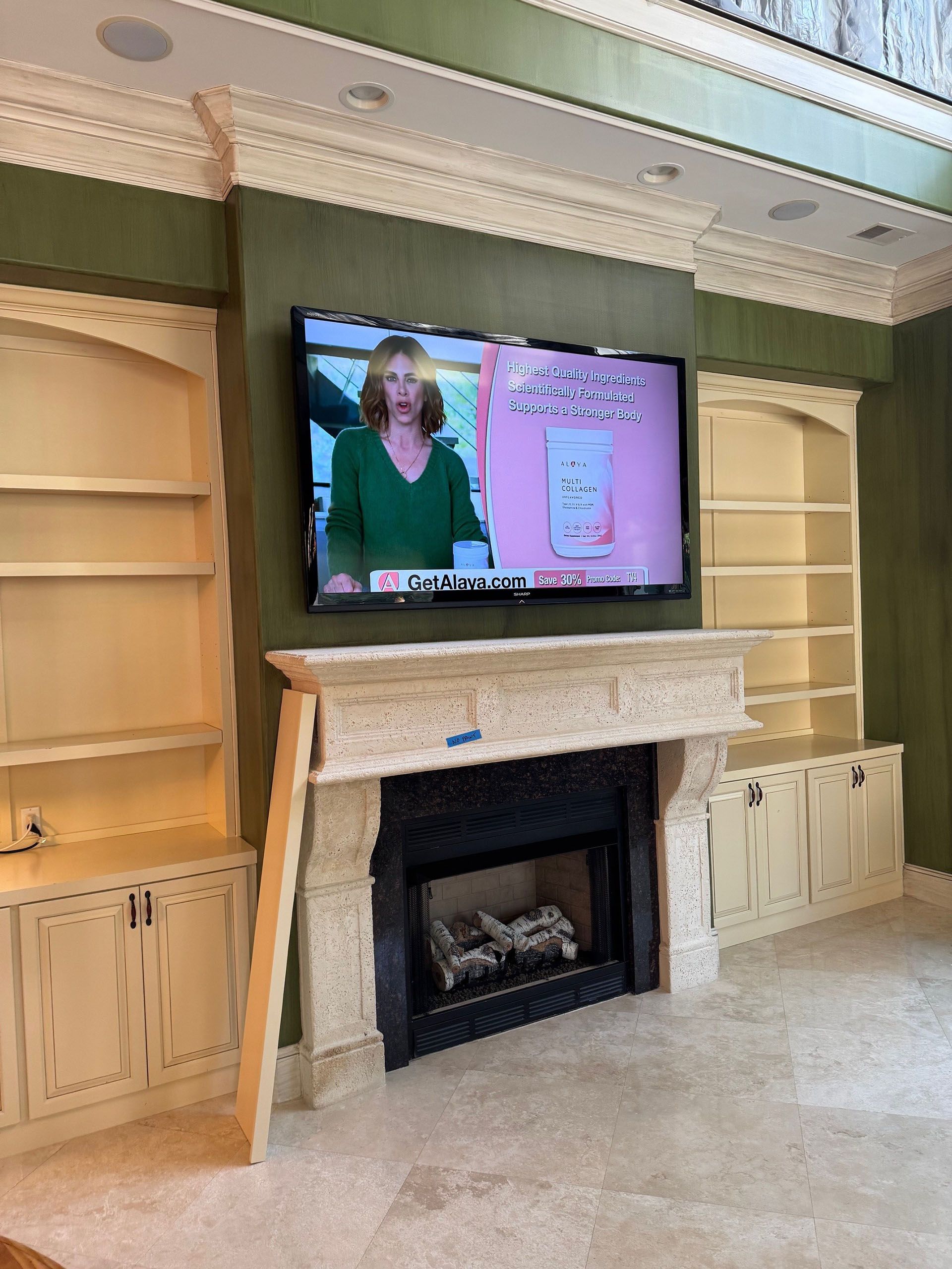 Wexford Home Remodel - Before: TV mounted above fireplace in a room with built-in bookshelves. A woman is on the TV screen.