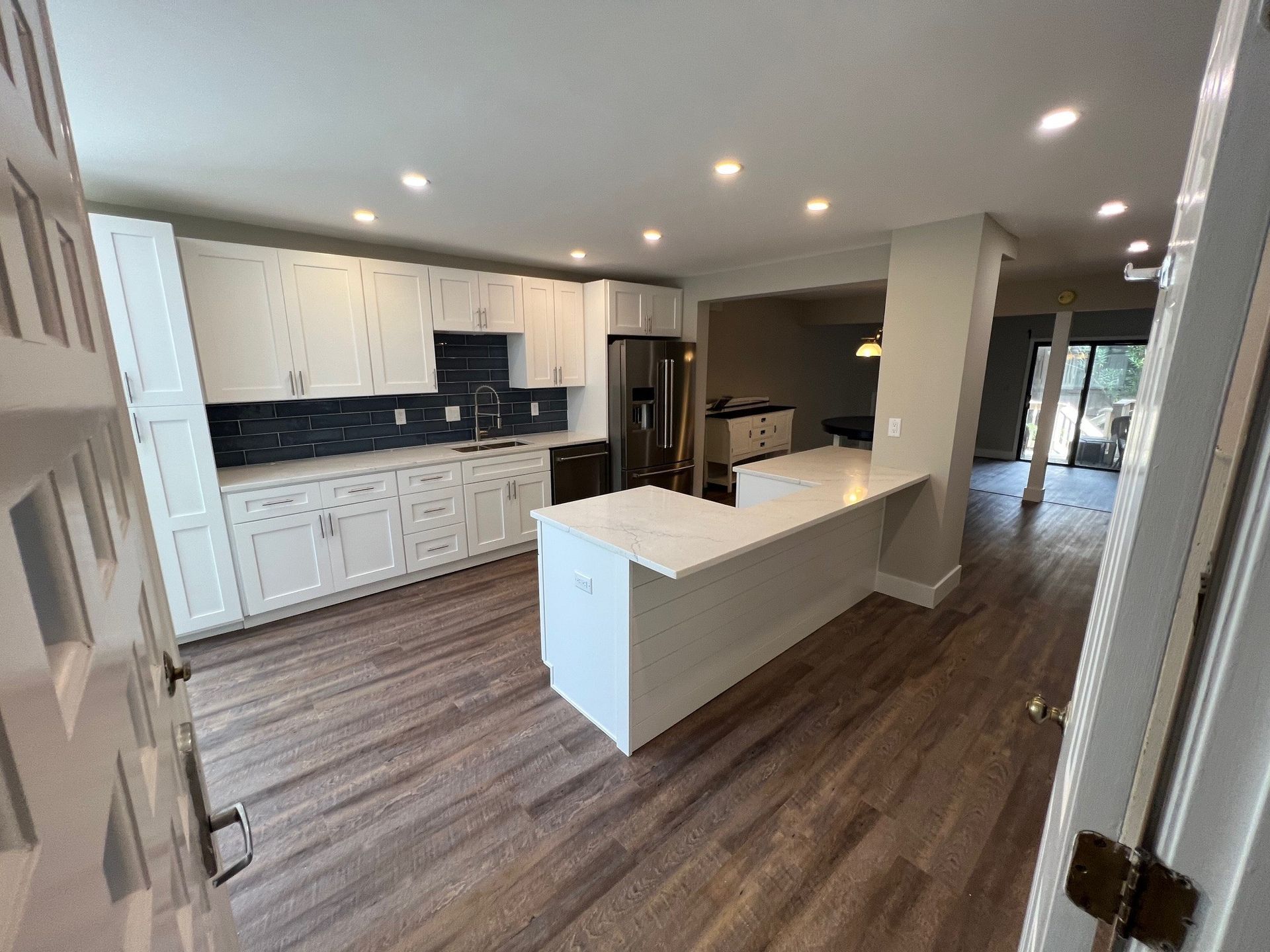 Newly renovated white kitchen with blue backsplash, stainless steel appliances, and island.