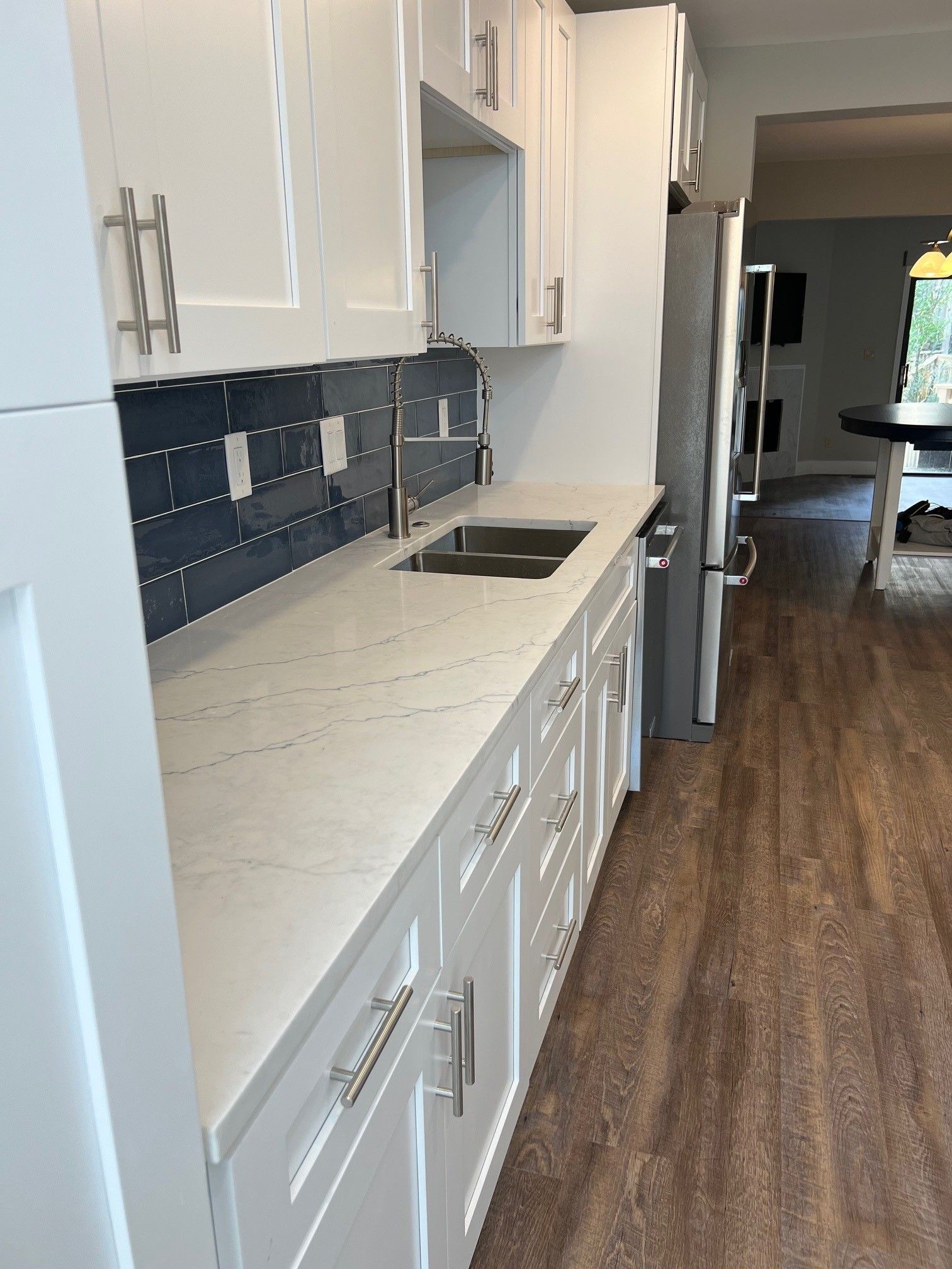White kitchen cabinets with light countertops and blue backsplash. Stainless steel appliances and sink.