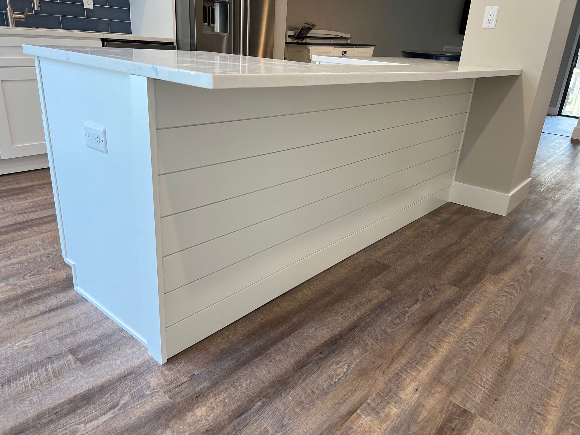 White kitchen island with a shiplap design and white countertop, set on wood flooring.