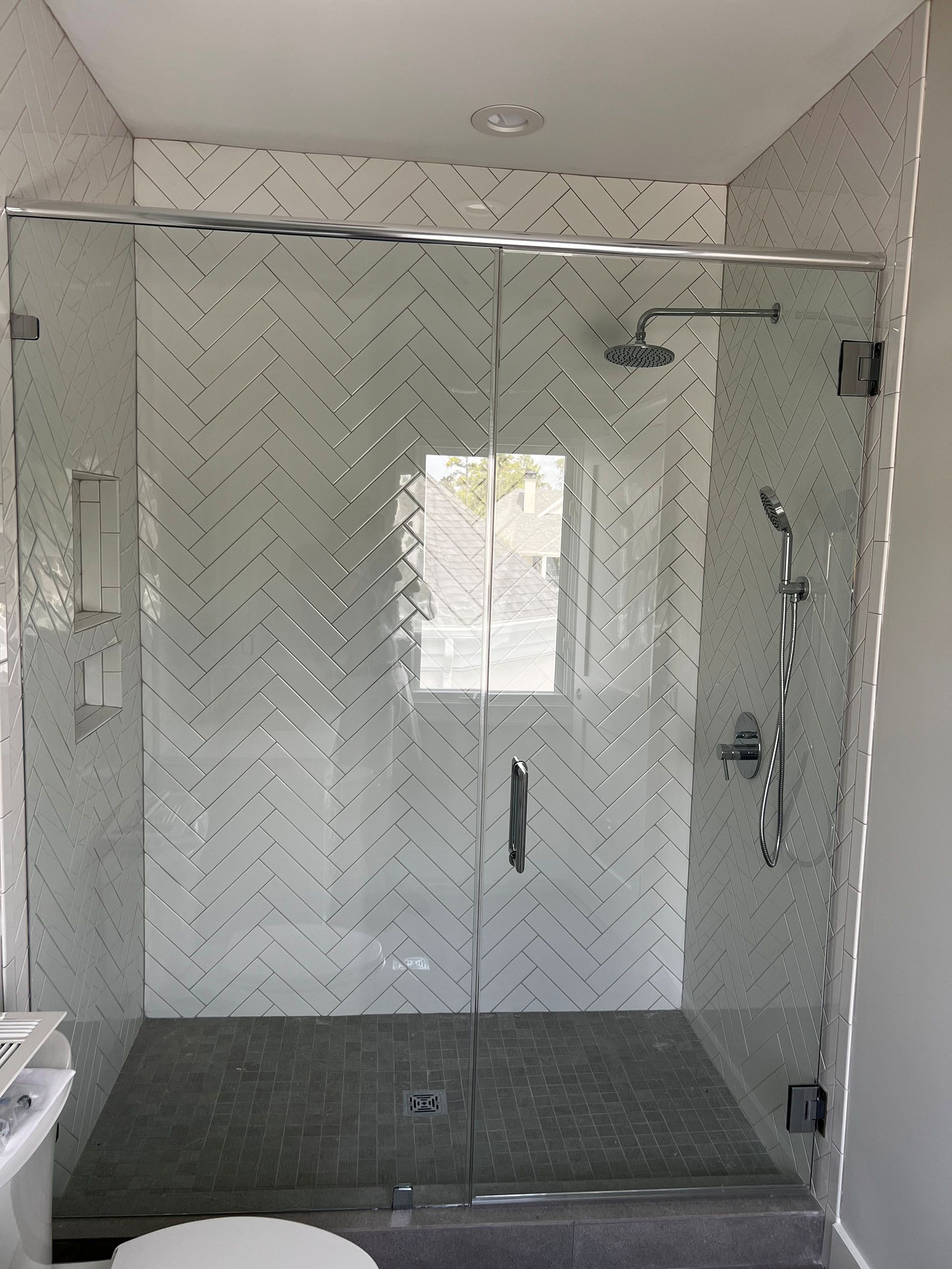 Miscellaneous Bathroom Projects - Glass shower doors with herringbone tile background, shower head, and gray tile floor.
