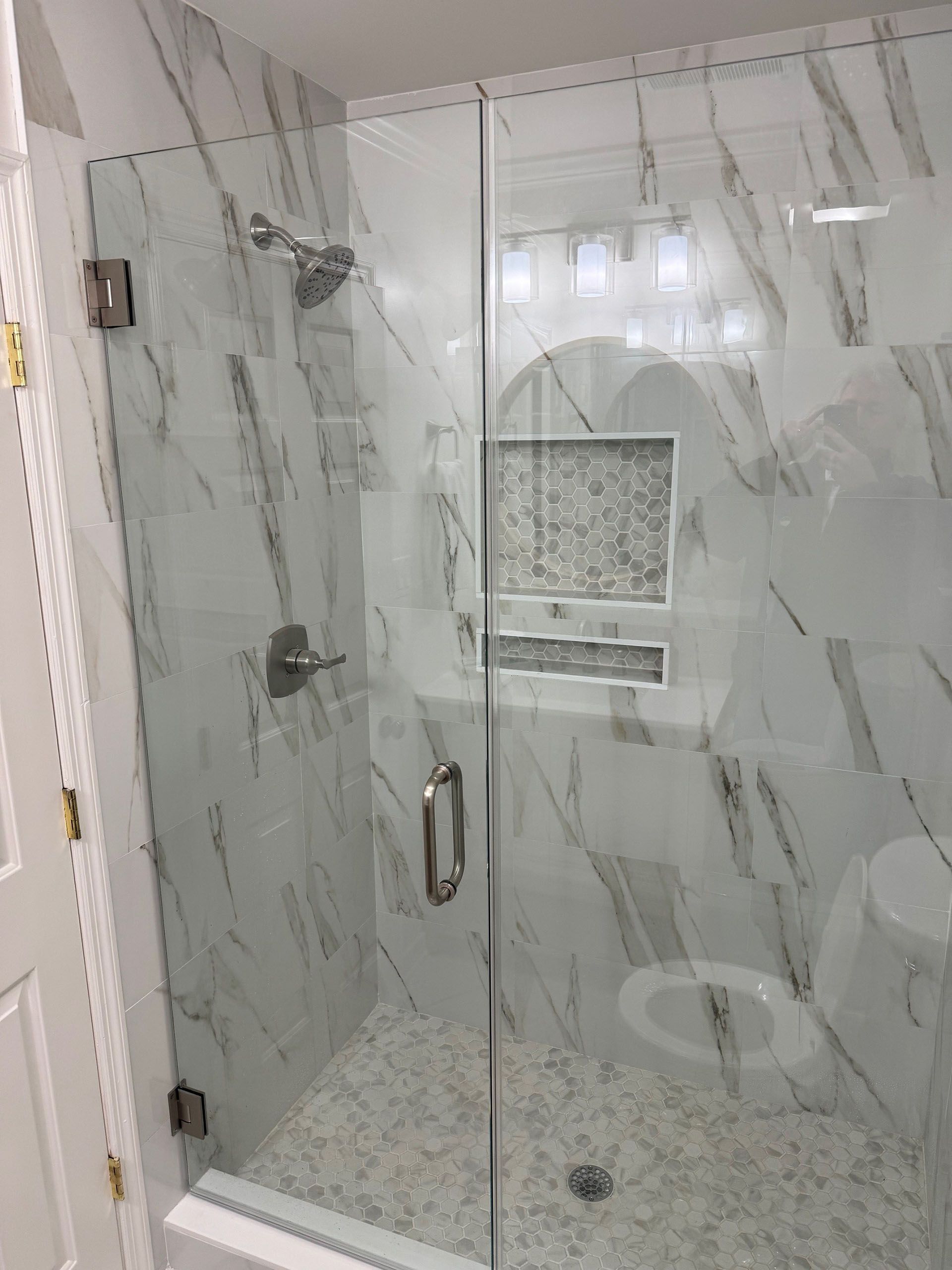 Miscellaneous Bathroom Projects - Glass shower enclosure with white marble-look tile, a showerhead, and a built-in shelf.