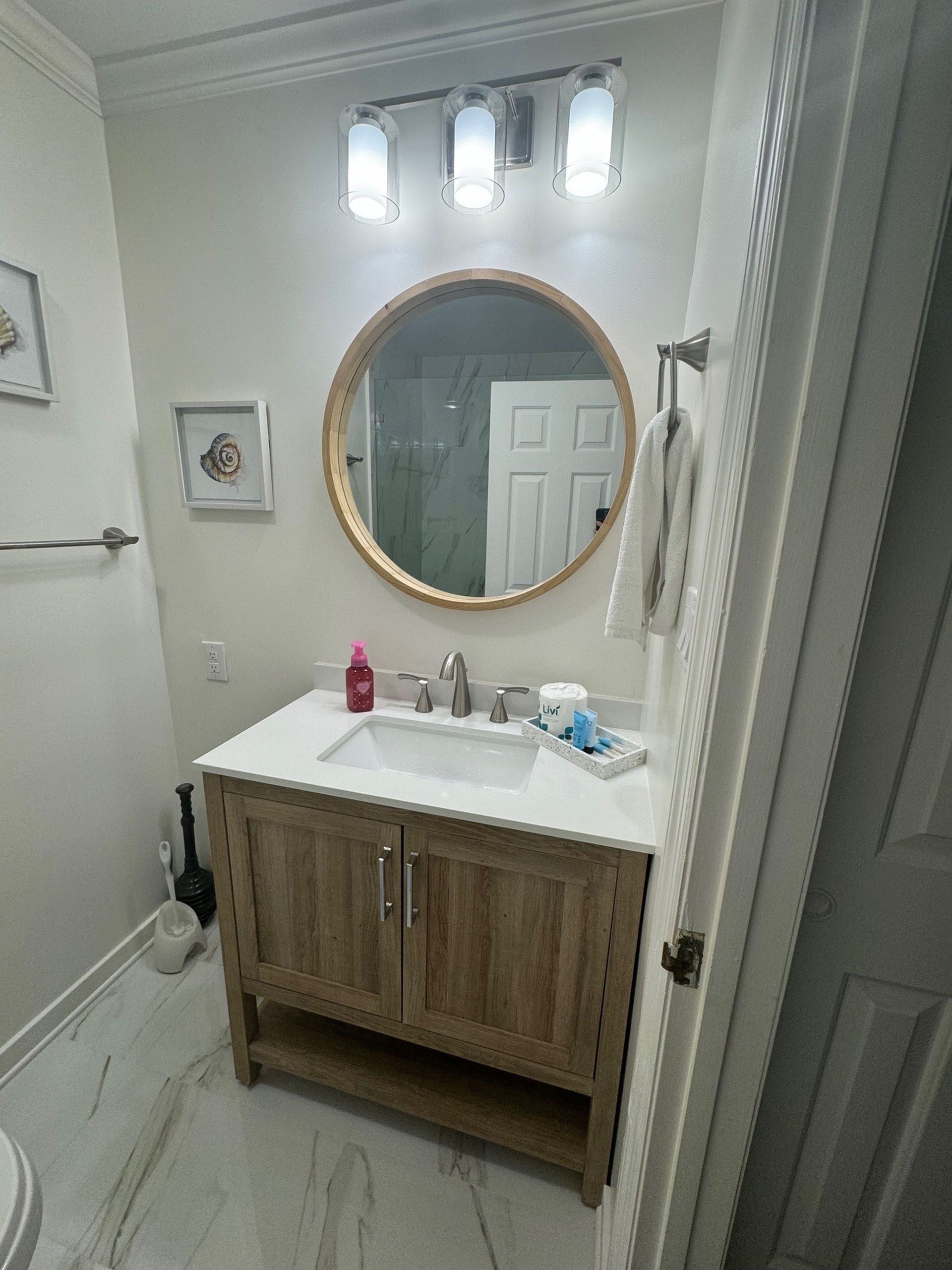 Miscellaneous Bathroom Projects - Bathroom with wood vanity, round mirror, white countertop, and white walls.