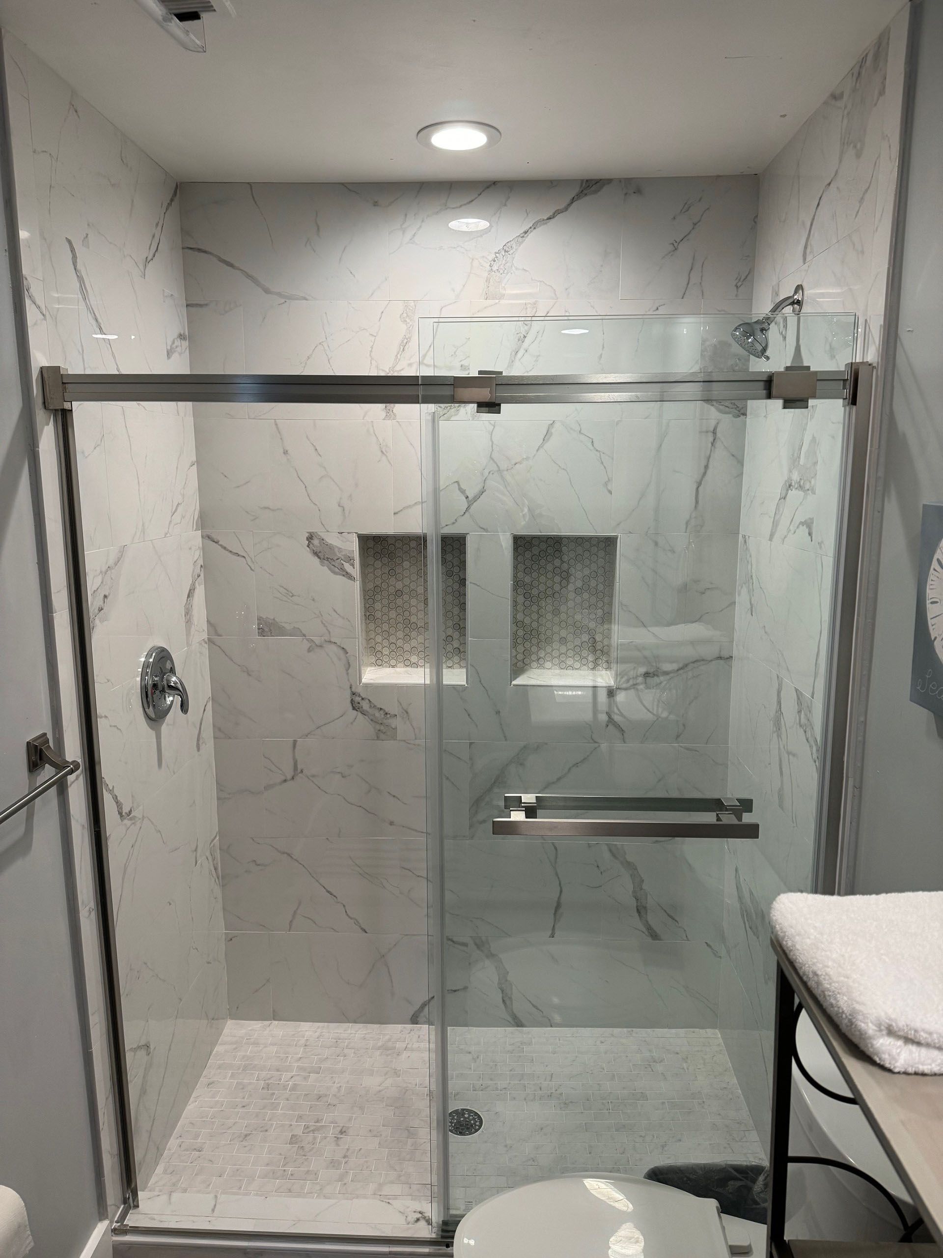 Miscellaneous Bathroom Projects - Modern shower with white marble-look tile, glass door, recessed shelves, and chrome fixtures.
