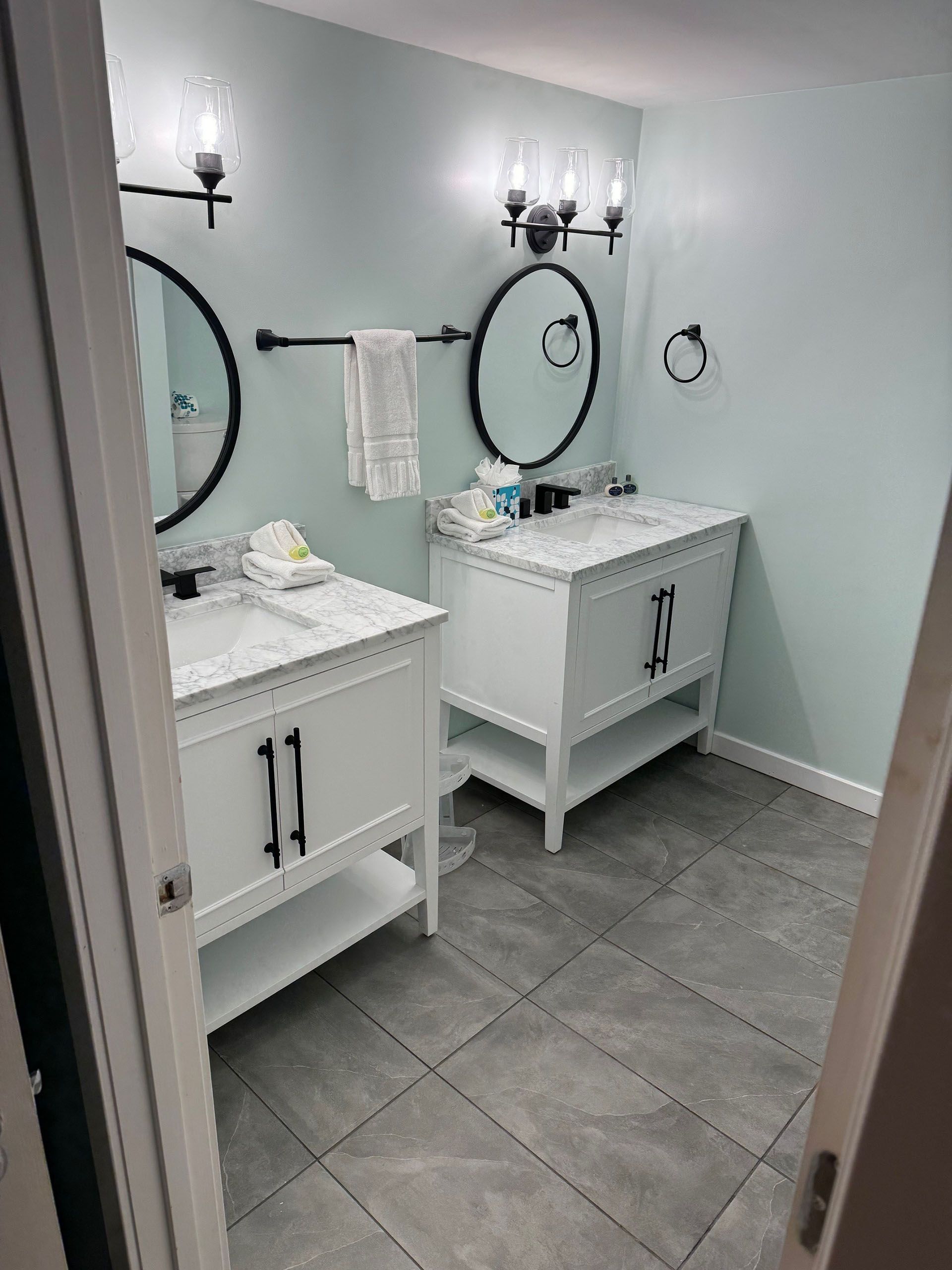 Miscellaneous Bathroom Projects - Bathroom with two white vanities, black mirrors, and light blue walls.