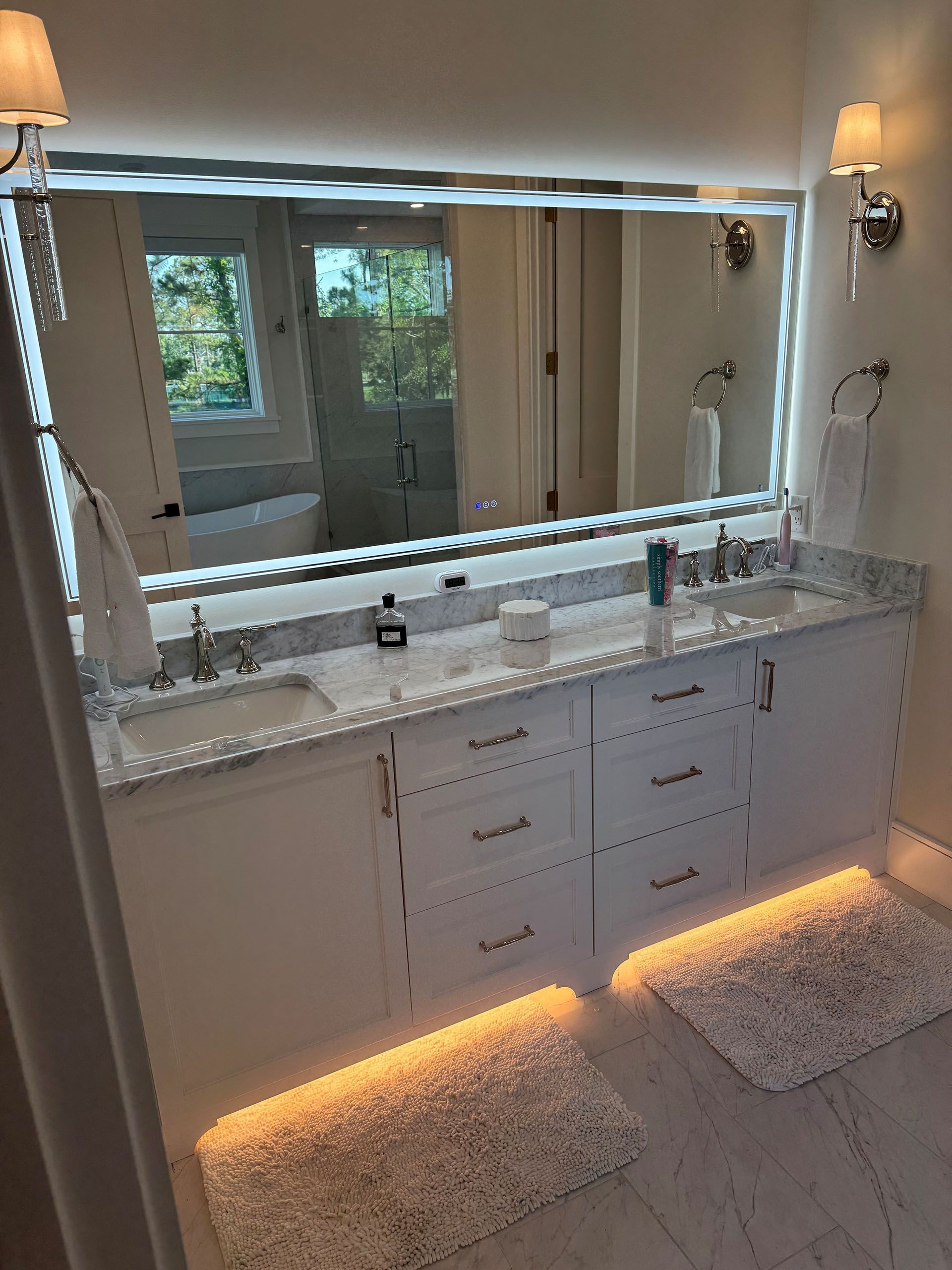 Miscellaneous Bathroom Projects - Bathroom vanity with lit mirror, white cabinets, marble countertop, and floor lighting.