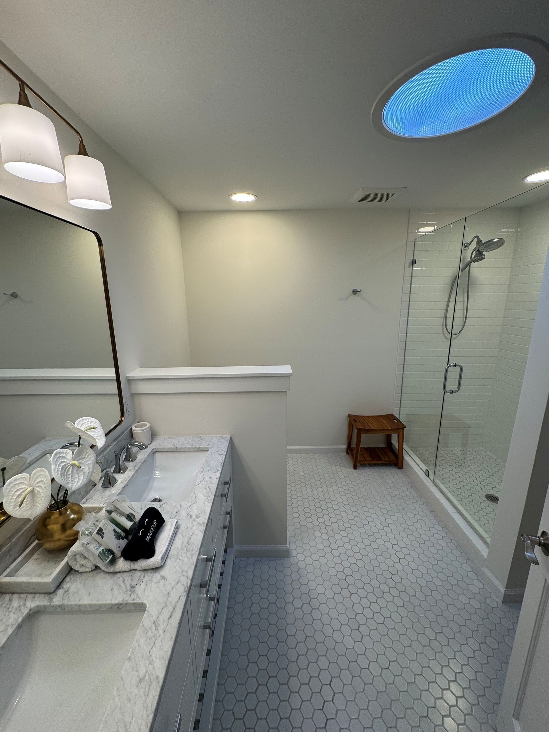 Miscellaneous Bathroom Projects - Modern bathroom with a double sink vanity, glass shower, and skylight. White and gray tones.