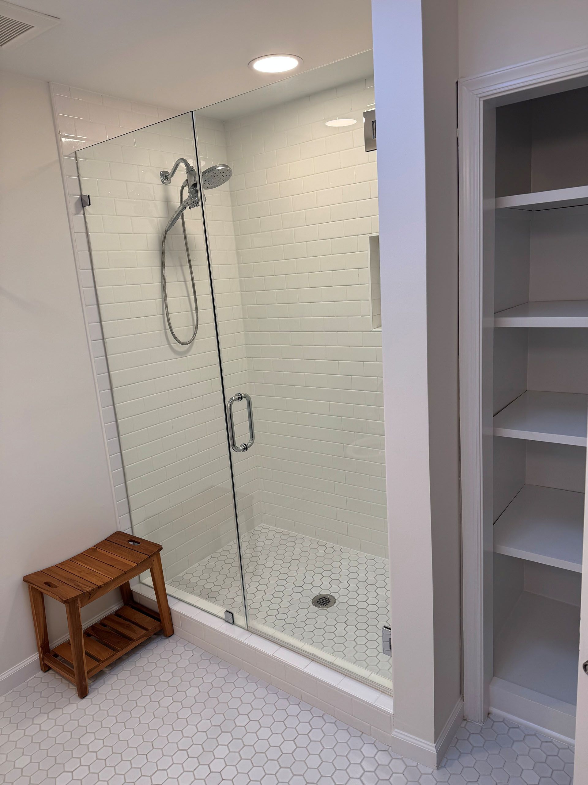 Miscellaneous Bathroom Projects - Modern white tiled bathroom with glass shower, wooden stool, and built-in shelves.