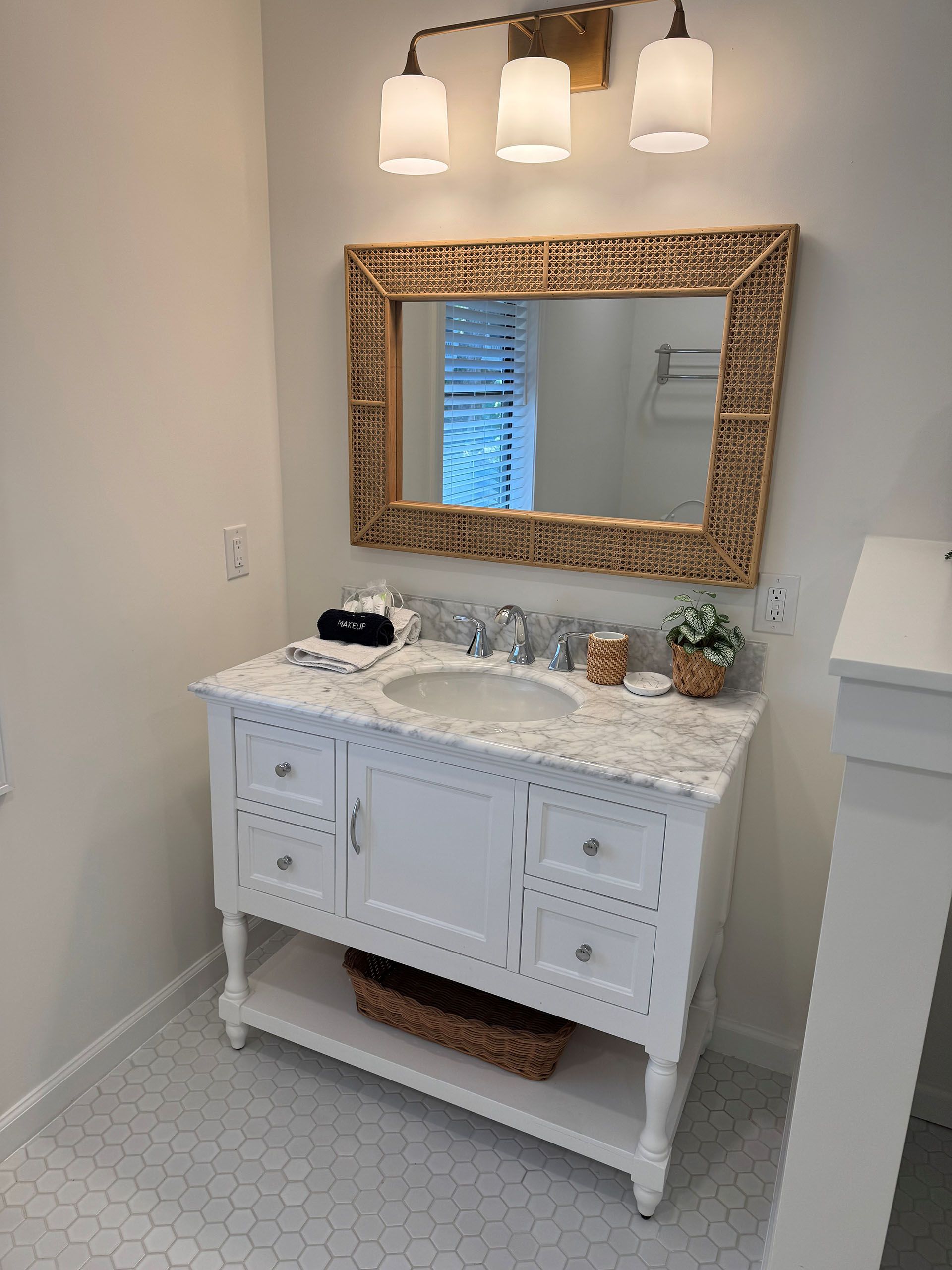 Miscellaneous Bathroom Projects - White bathroom vanity with marble top, woven mirror, and hexagon tile floor.