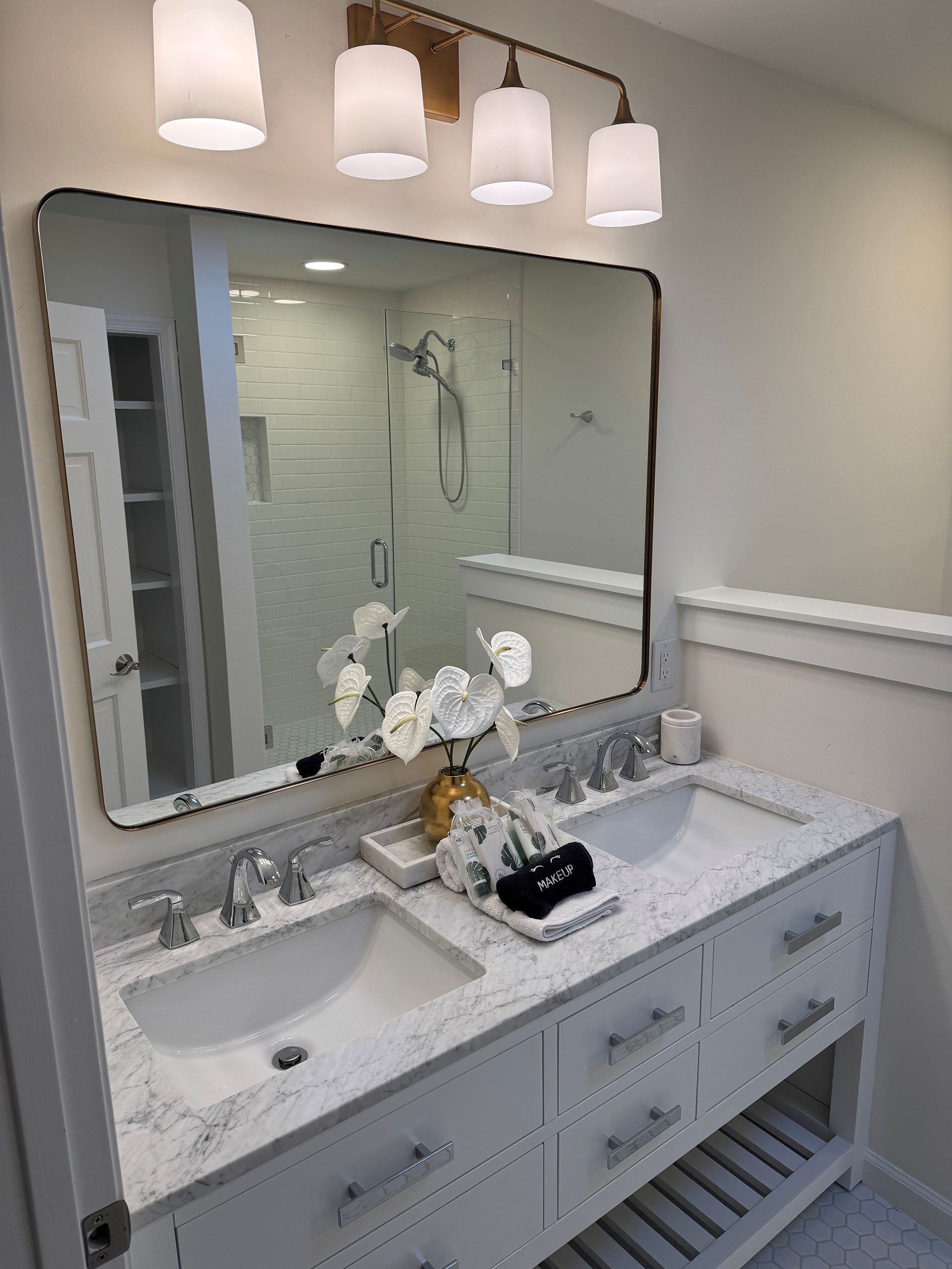 Miscellaneous Bathroom Projects - Bathroom with double sinks, large mirror, white cabinetry, and a gold-toned light fixture.