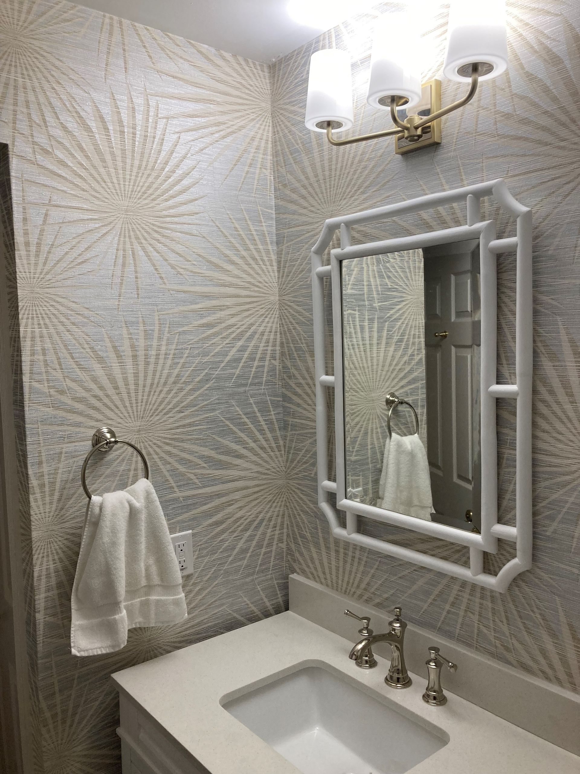 Bathroom with white vanity, patterned wallpaper, white framed mirror, and chrome fixtures.