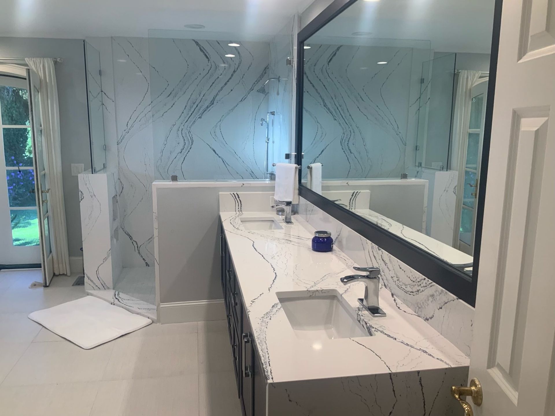 Modern bathroom with marble patterned walls and countertop, double sinks, and large mirror.