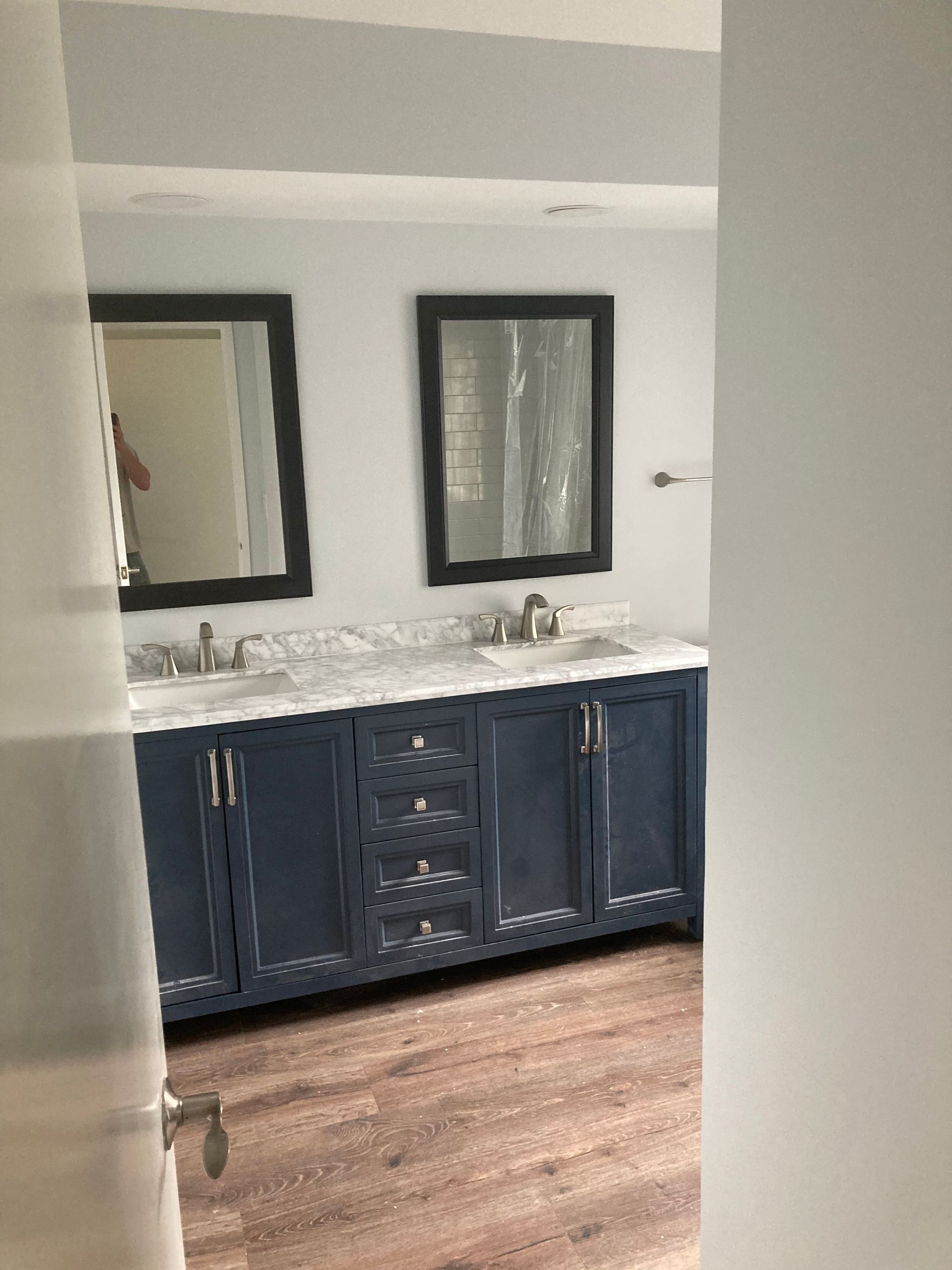 Blue vanity with two mirrors and sinks in a bathroom. Brown flooring and white walls.