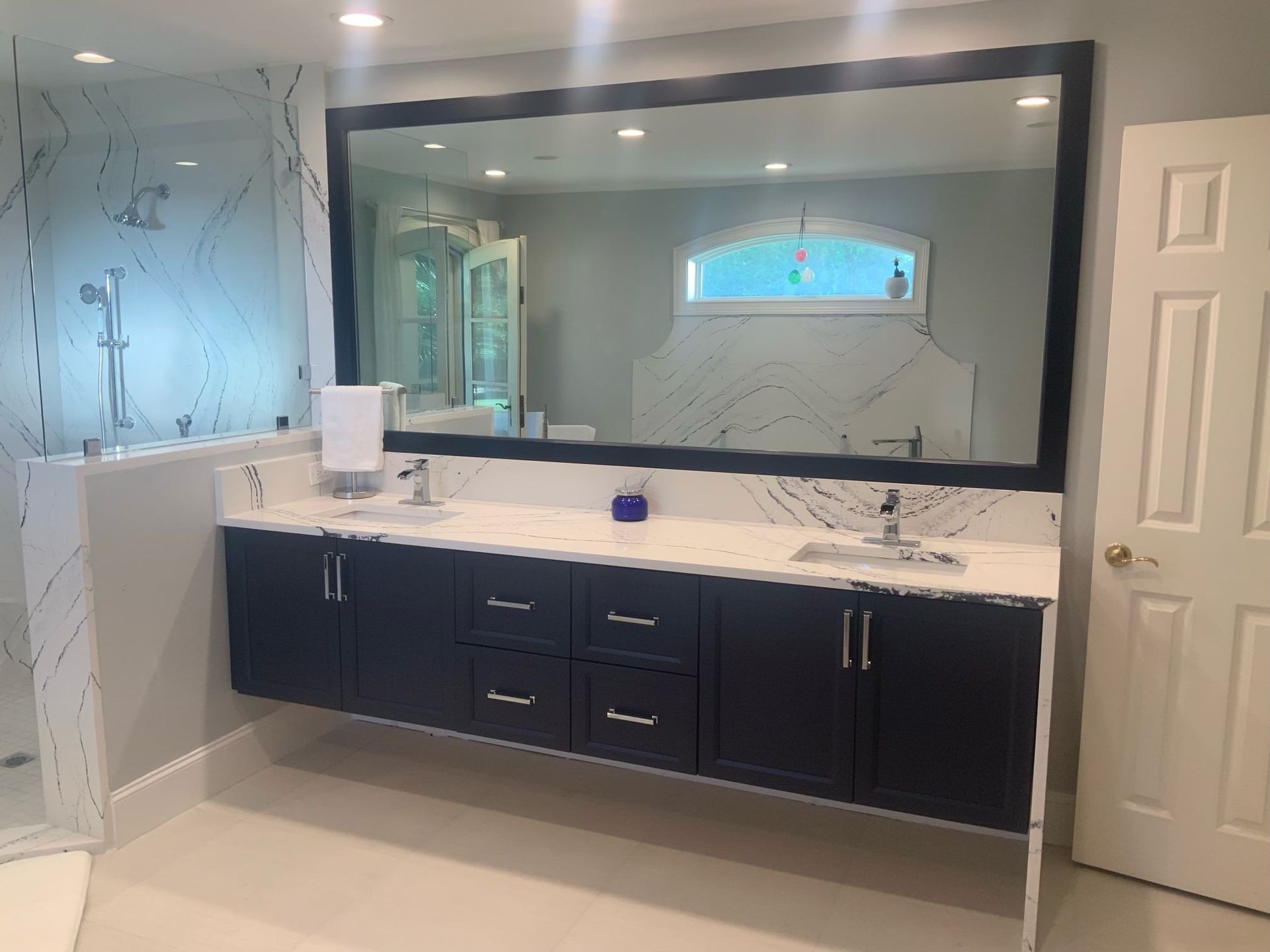 Modern bathroom with dark blue floating vanity, large mirror, and marble accents.