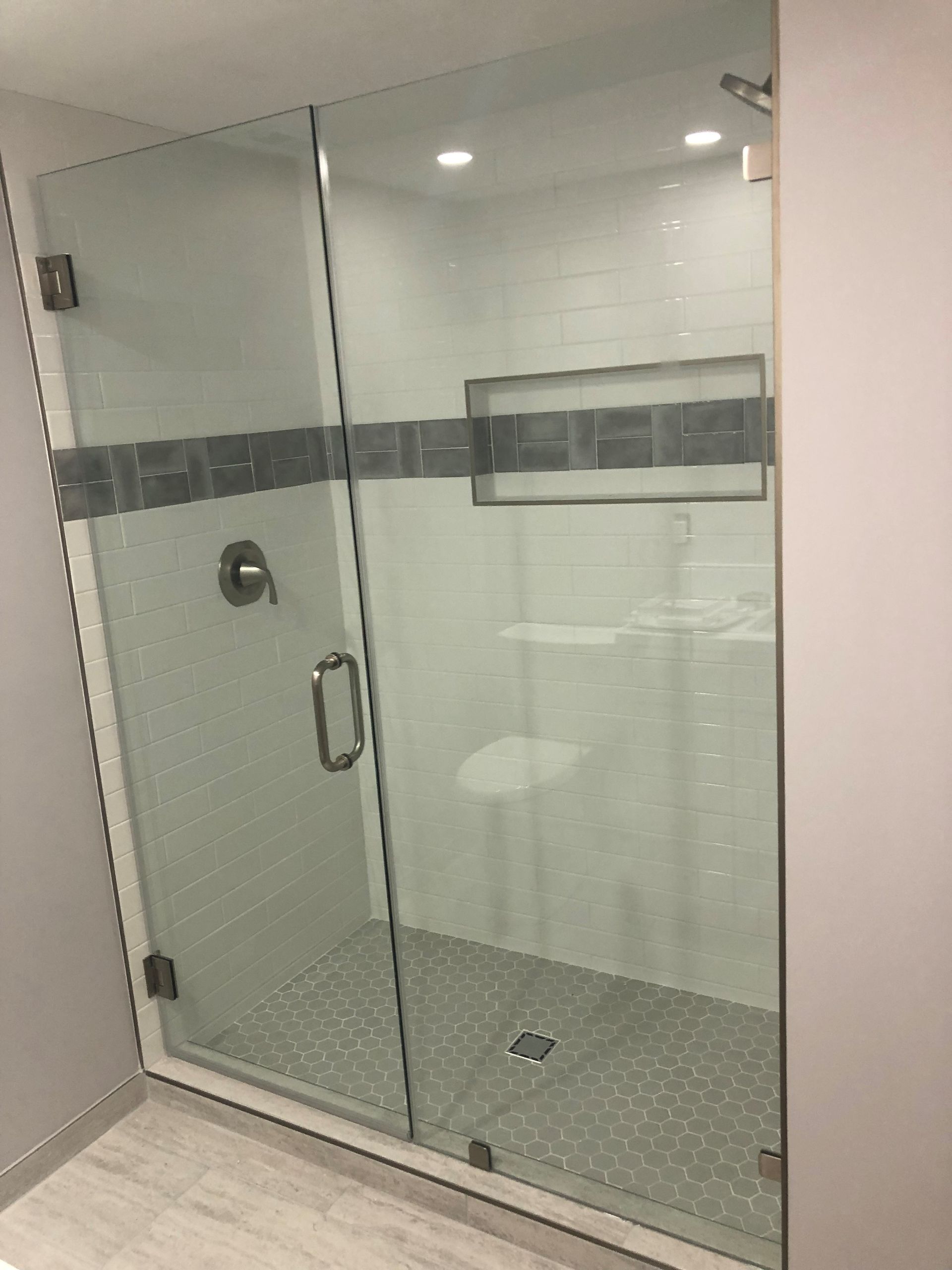 Glass shower enclosure with gray tile accents and recessed shelf.