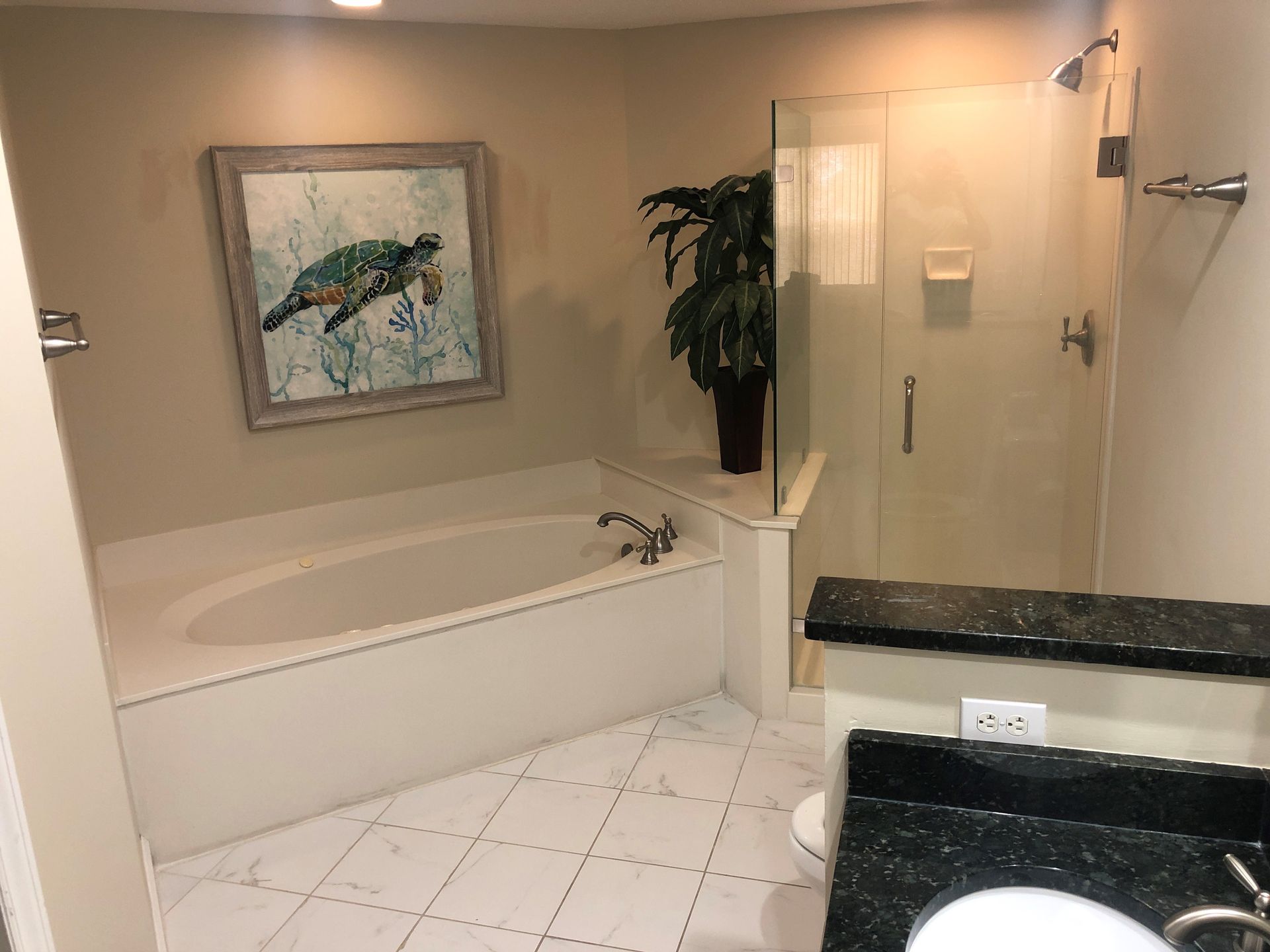 Bathroom with a white bathtub, glass shower, and turtle artwork; light tile floor.