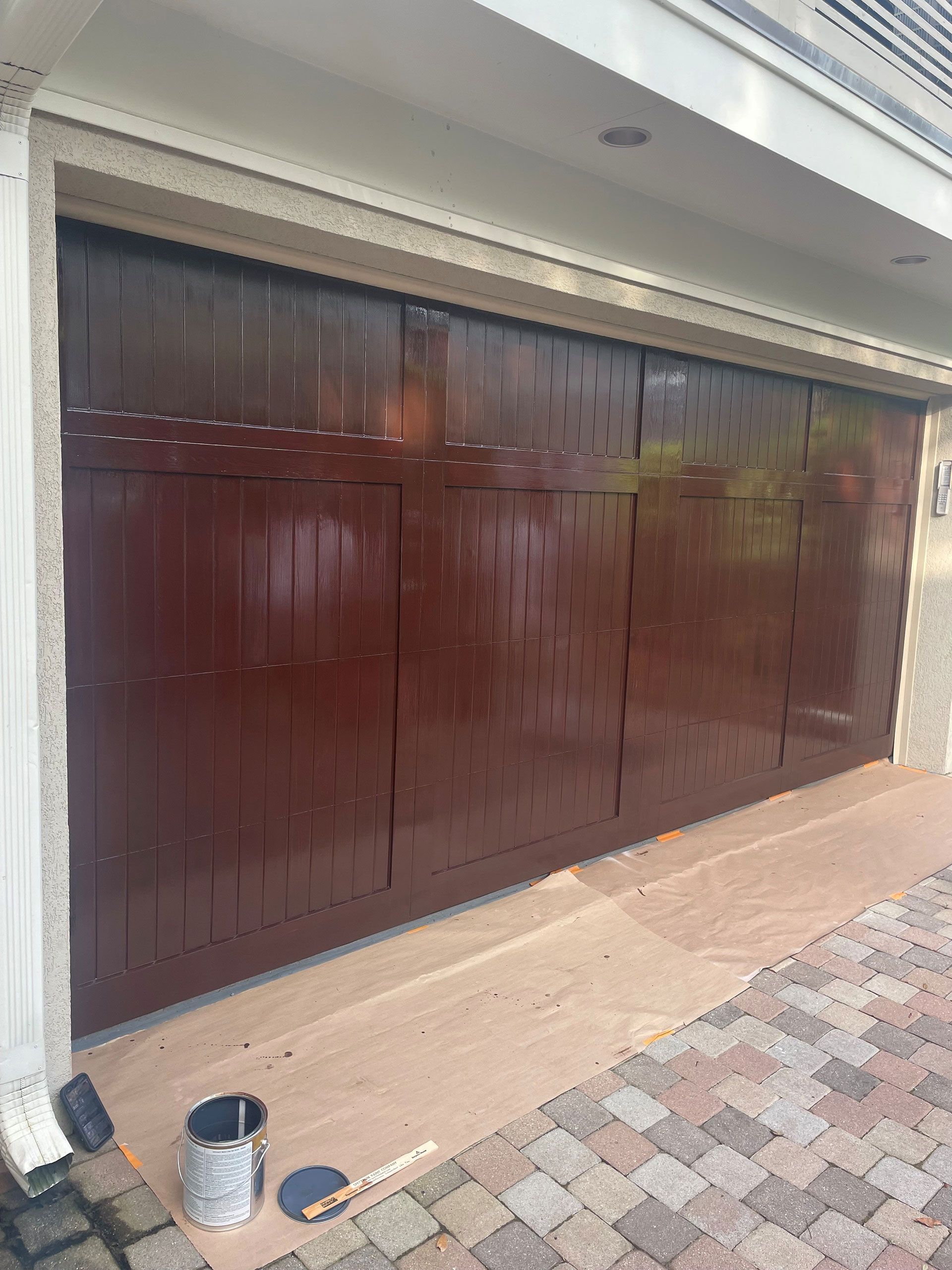 Brown painted garage door with a paint can and supplies on the ground.