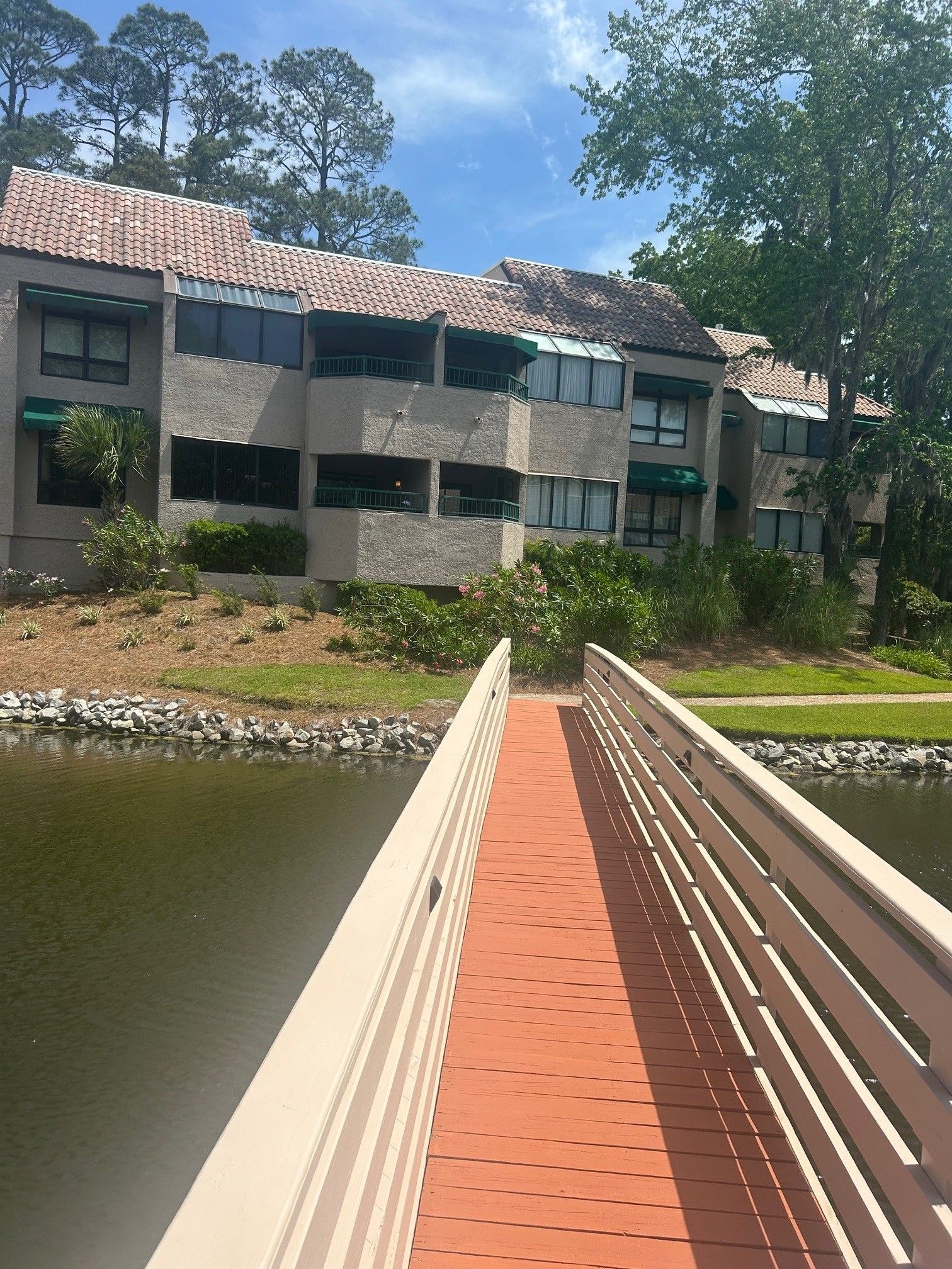 Wooden bridge leading to a multi-story building with green awnings, set on a lake.
