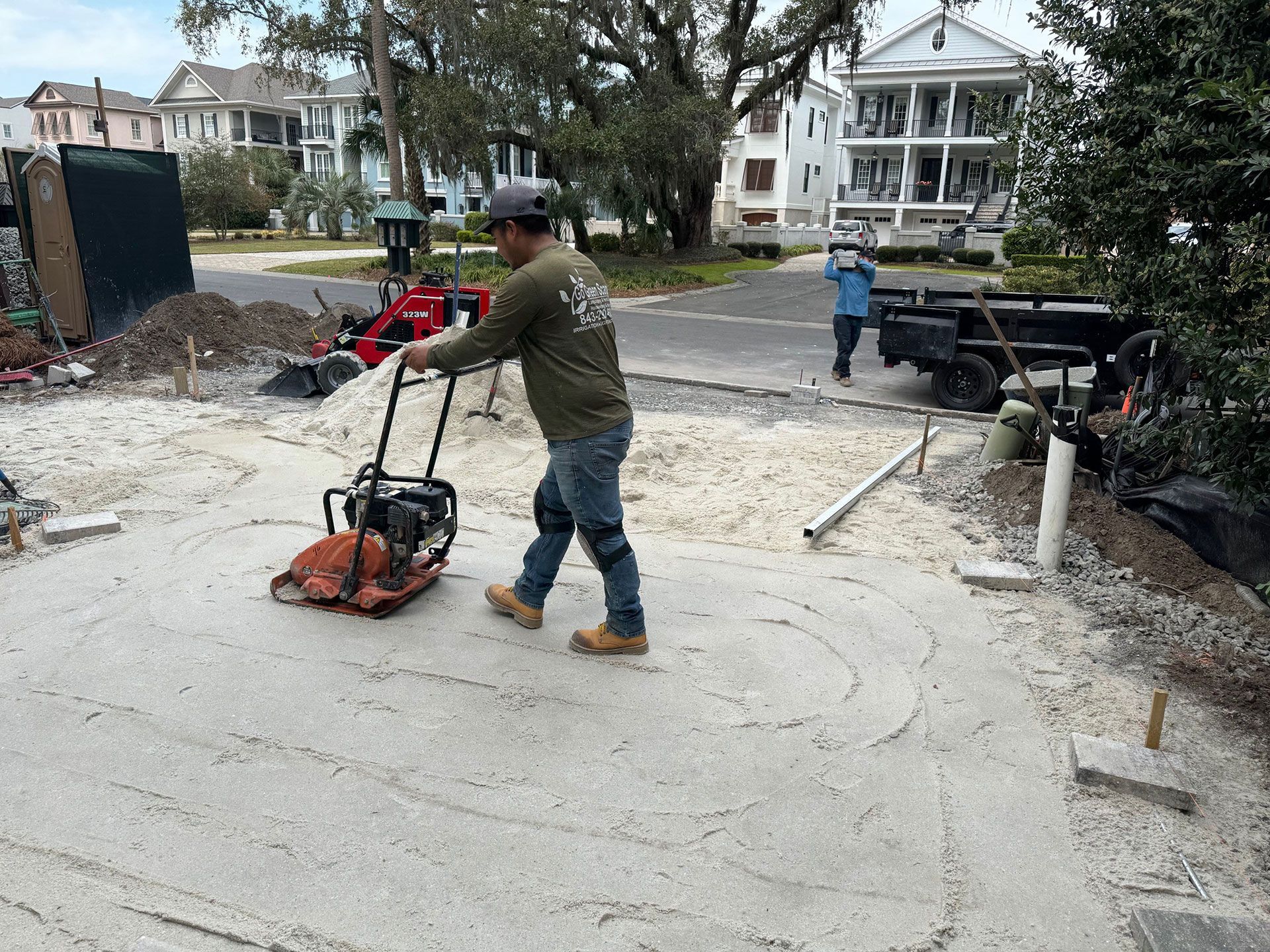 Man compacts sand with a plate compactor on a construction site.