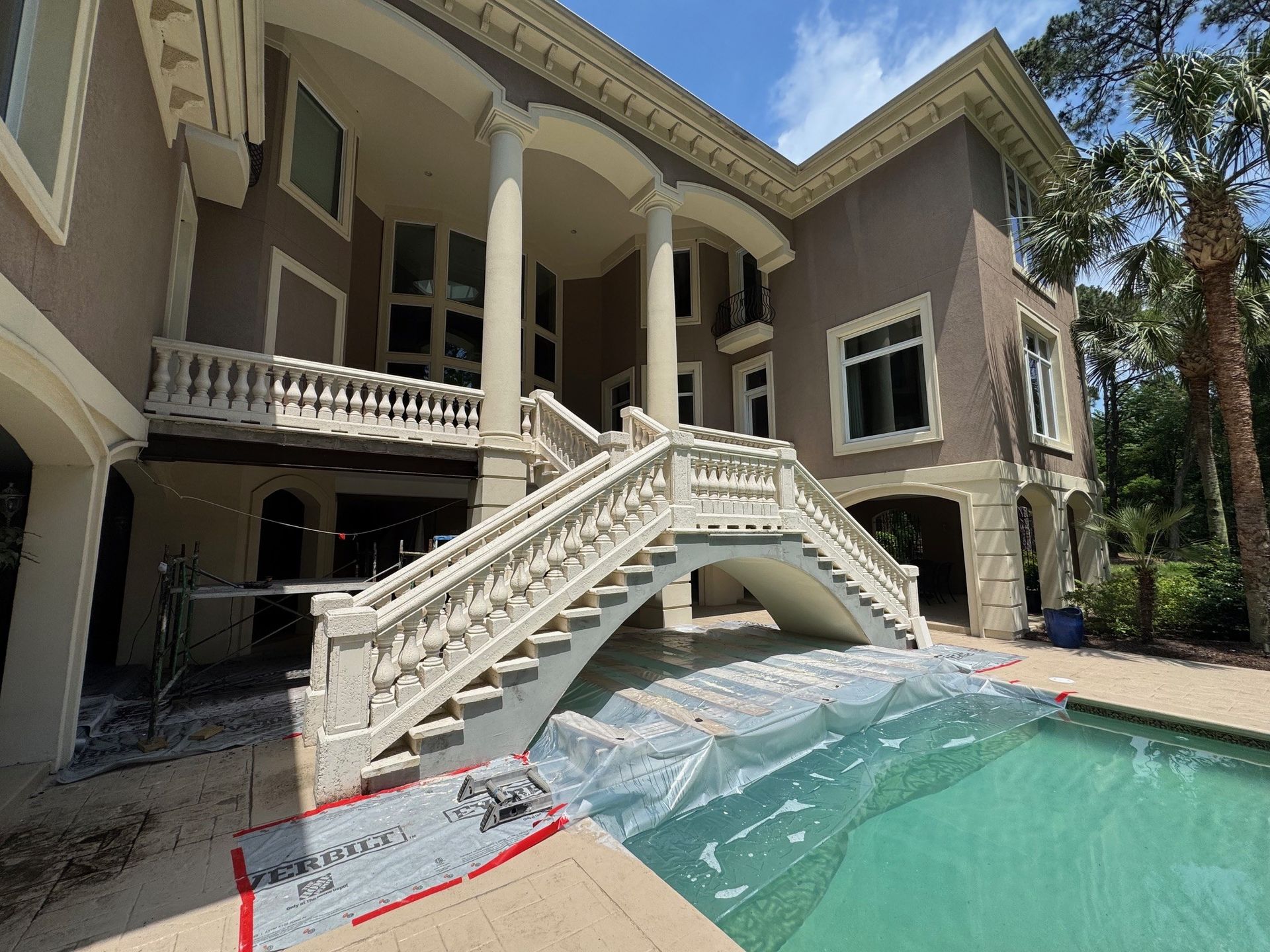 Beige and white two-story house with a pool. Stairs and balcony lead to the entrance.