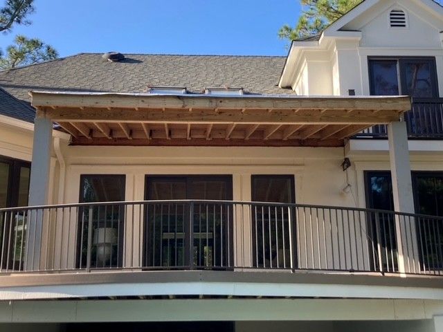 A partially constructed outdoor deck with a gray railing, attached to a white building with dark windows.