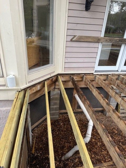 Deck under construction next to a house with exposed joists, boards, and a drainage pipe.