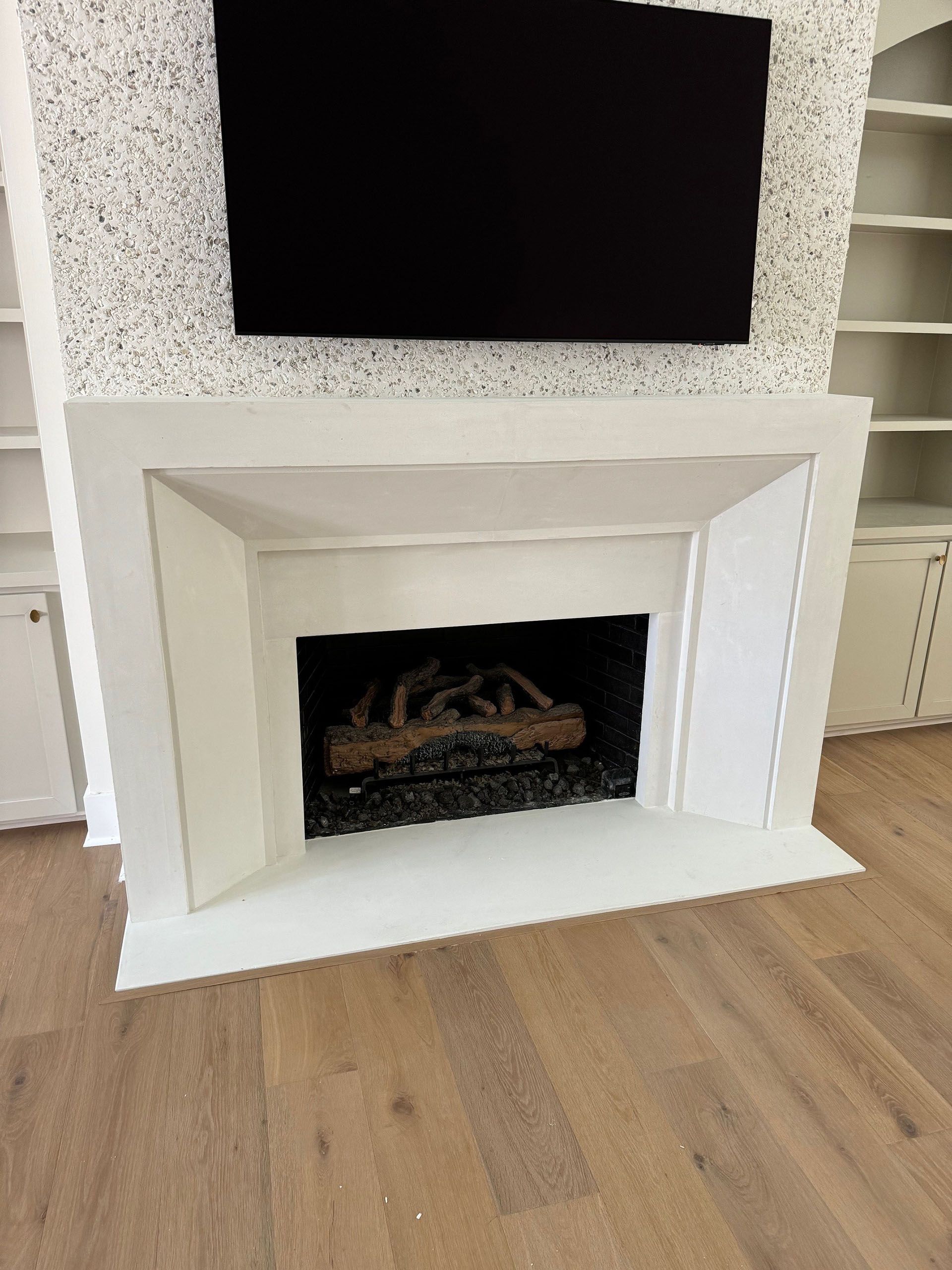 Miscellaneous Fireplace Projects - White fireplace with black TV above, flanked by white built-in shelves, on wood floor.