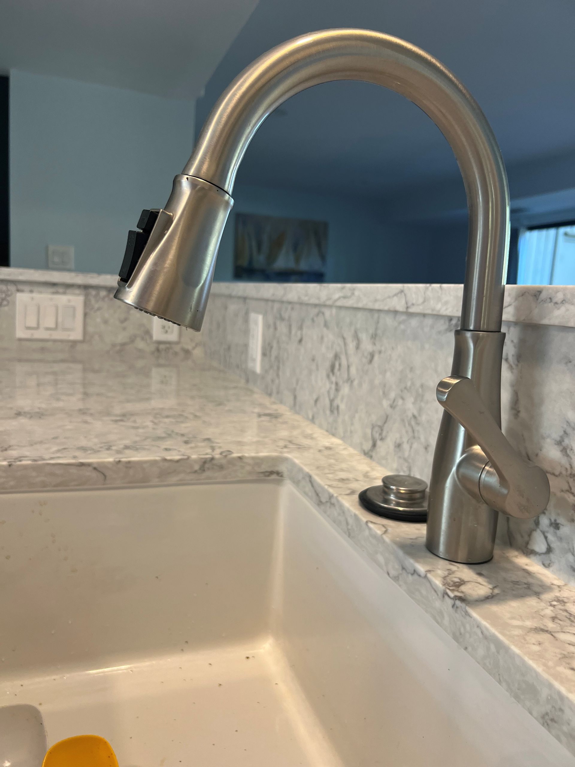 Stainless steel kitchen faucet over white sink on a marble countertop.