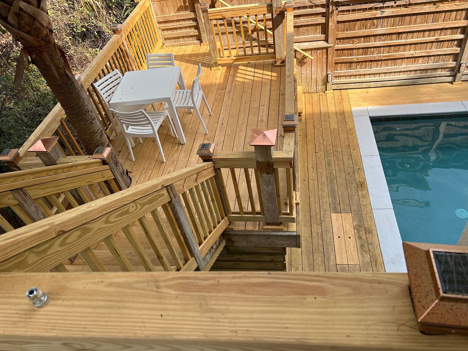 Wooden deck with stairs, table, chairs, and pool.
