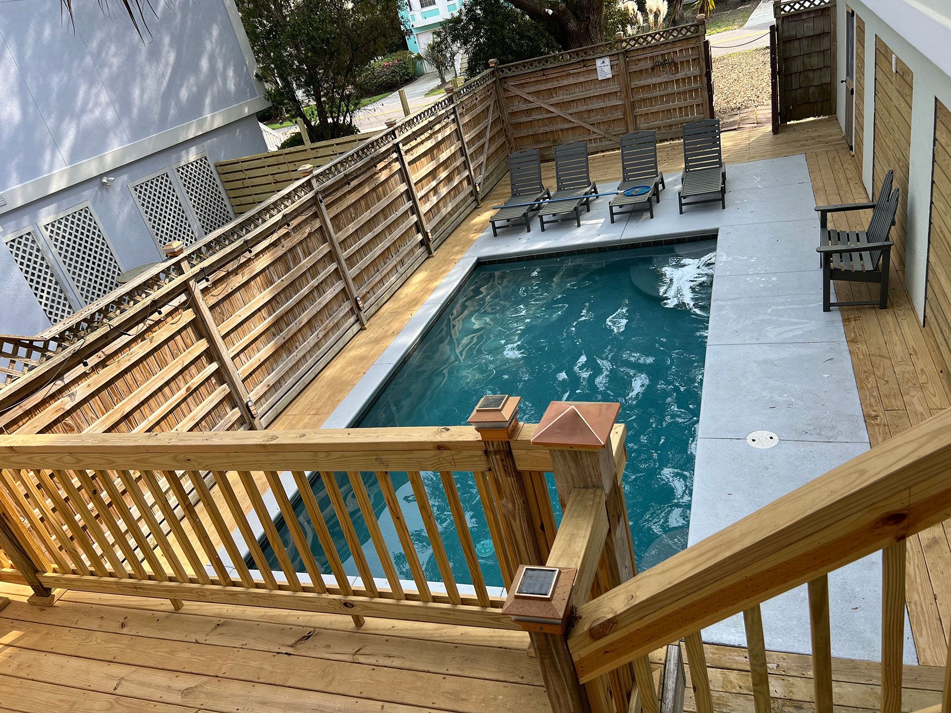 Pool area with wooden deck and fence, lounge chairs, and building.