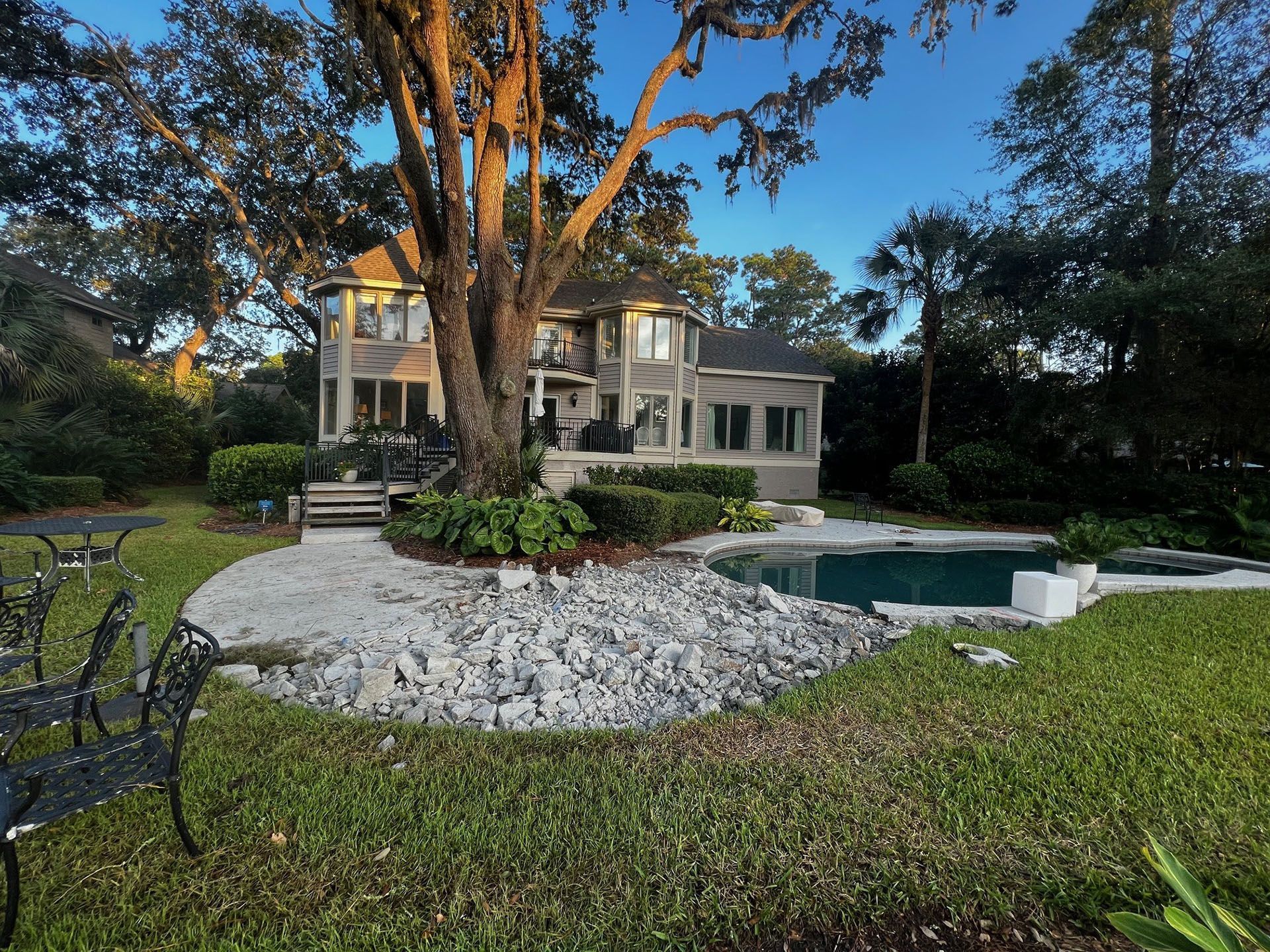 Miscellaneous Pool Projects - Two-story house with pool, shaded by large tree, surrounded by greenery and rocks.