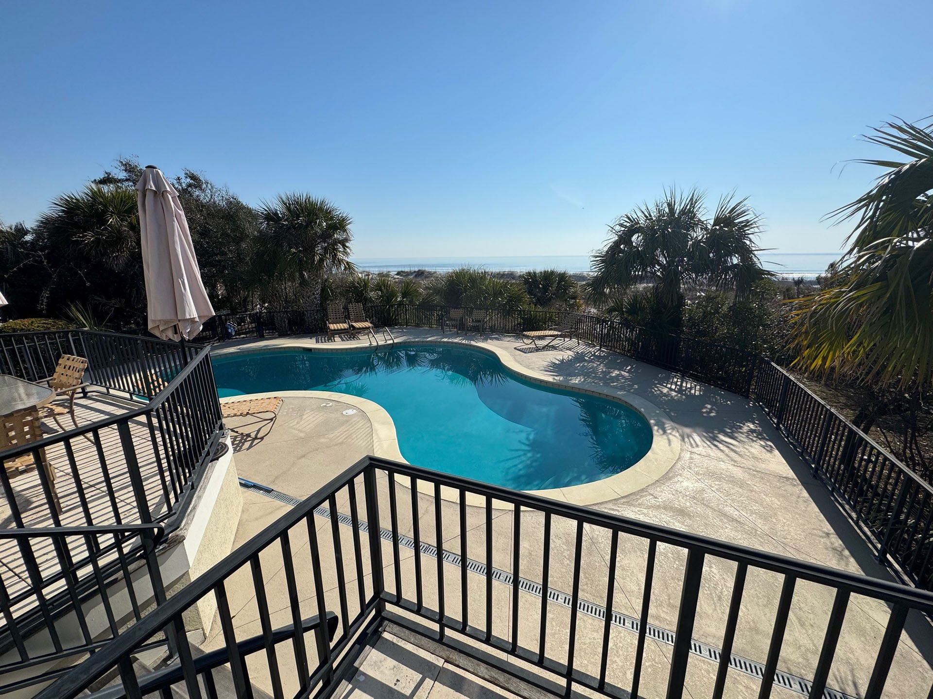 Miscellaneous Pool Projects - A pool with turquoise water, a patio, and a view of the ocean on a sunny day.