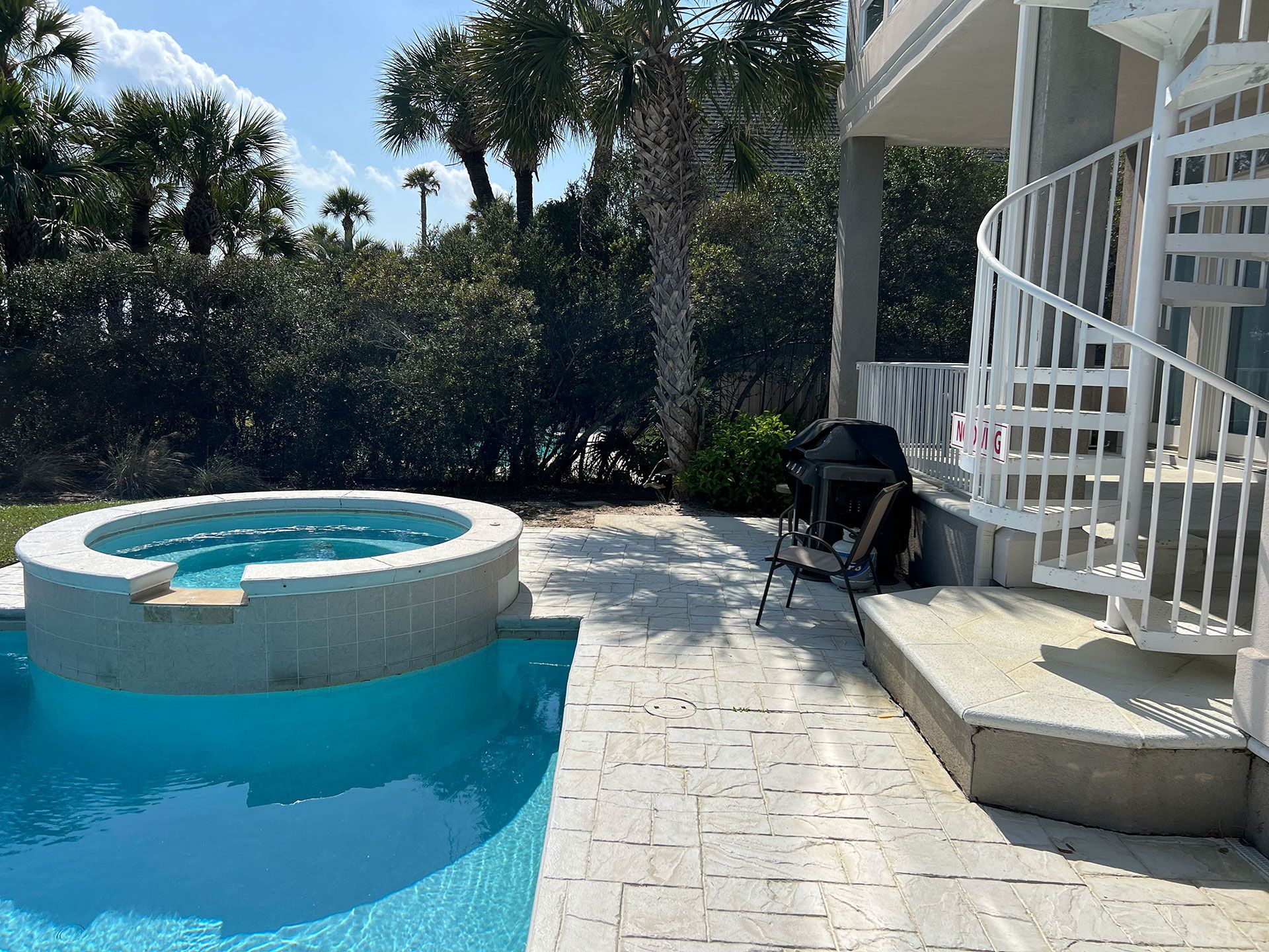 Swimming pool with attached hot tub, patio, spiral staircase, and grill near trees.