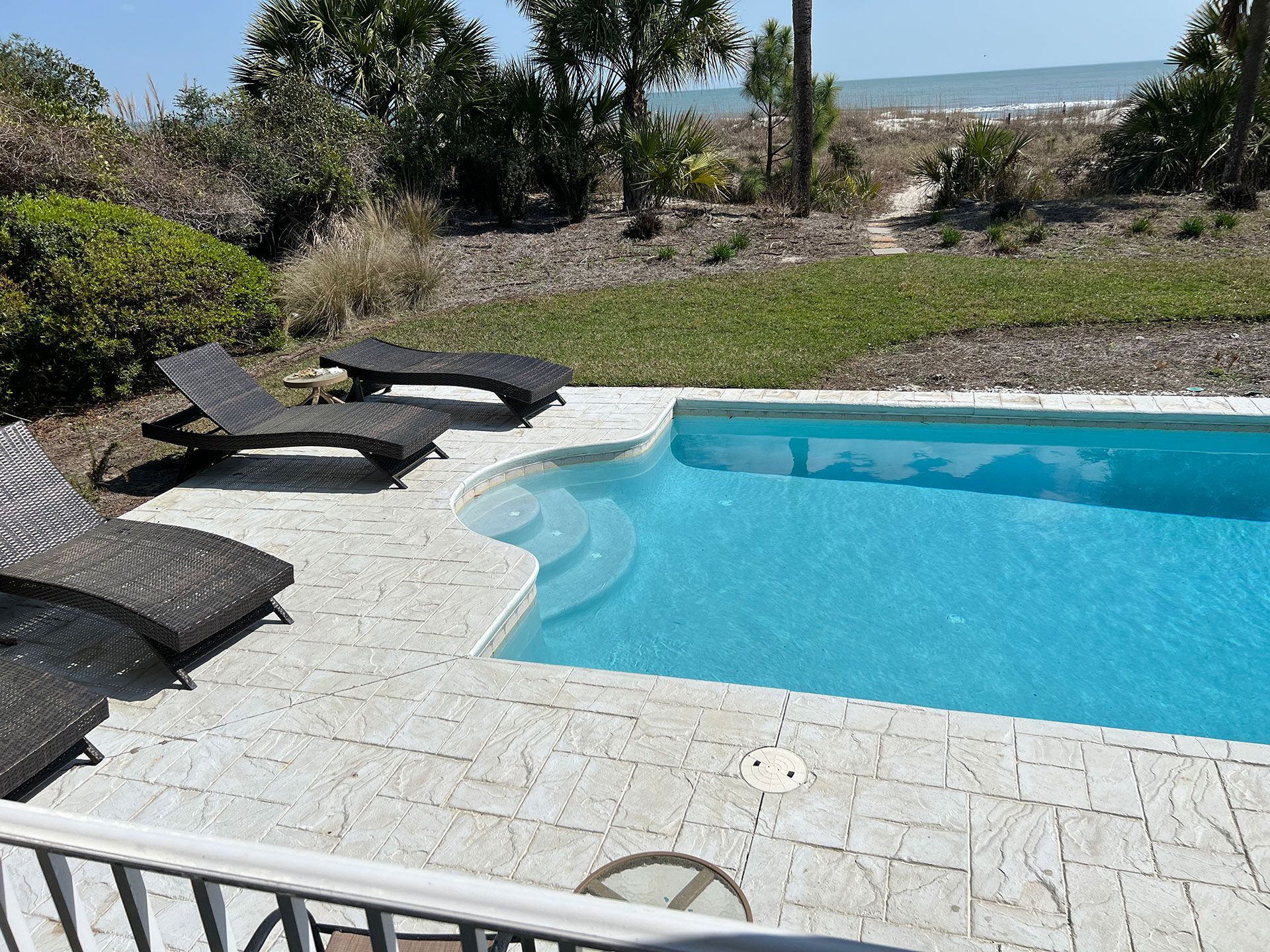 Poolside scene with chaise lounges, clear water, and a path to the beach.