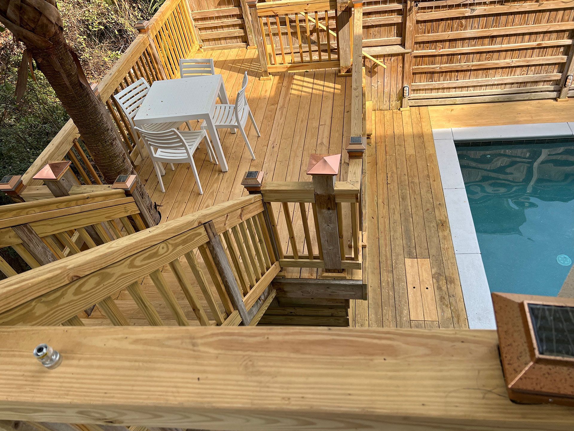 Wooden deck with stairs leads to a pool. A table and chairs sit on the deck.