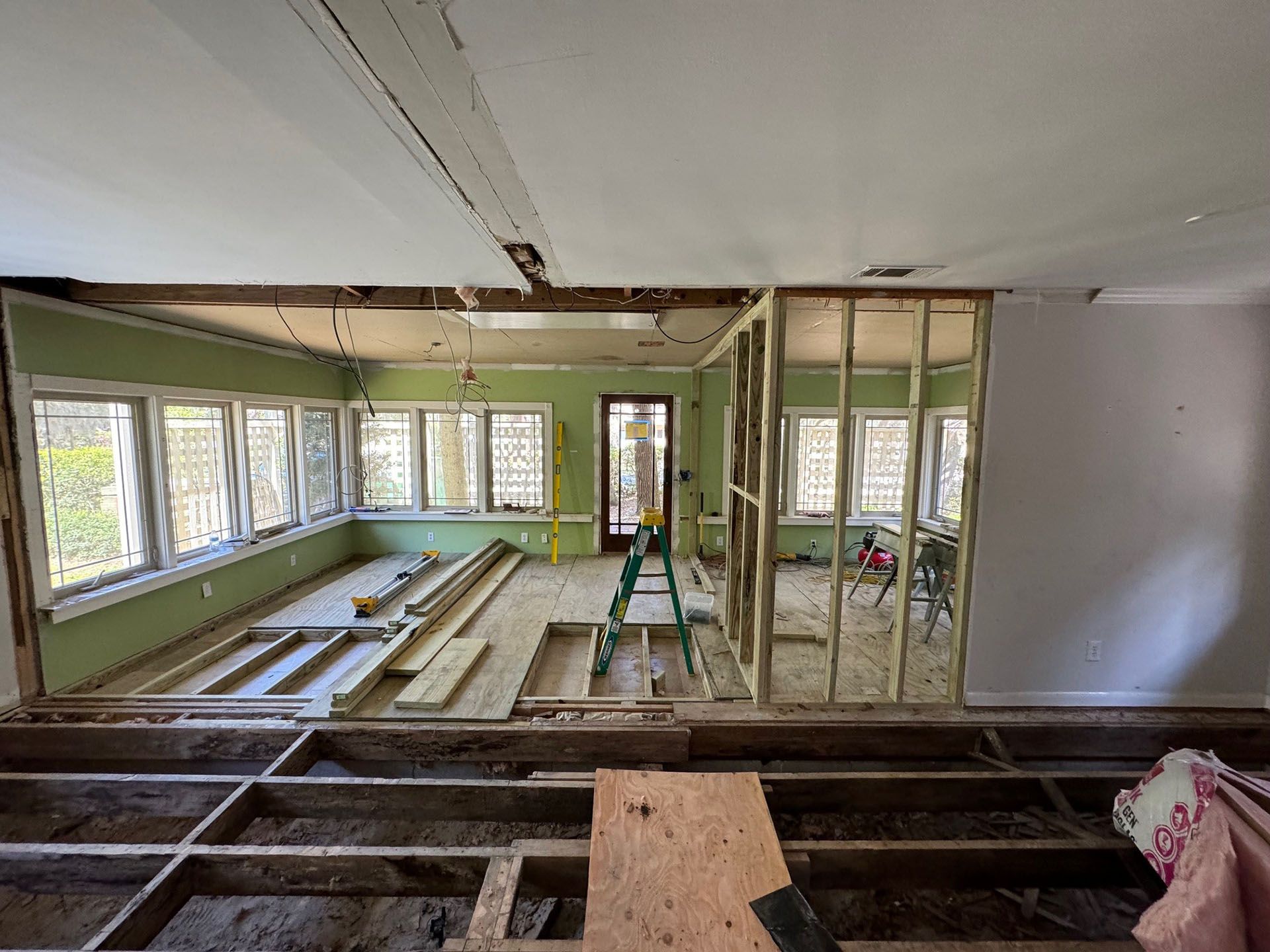 Termite Damage - Room undergoing renovation with exposed framing, floors, and drywall. Green walls, windows, and a doorway.
