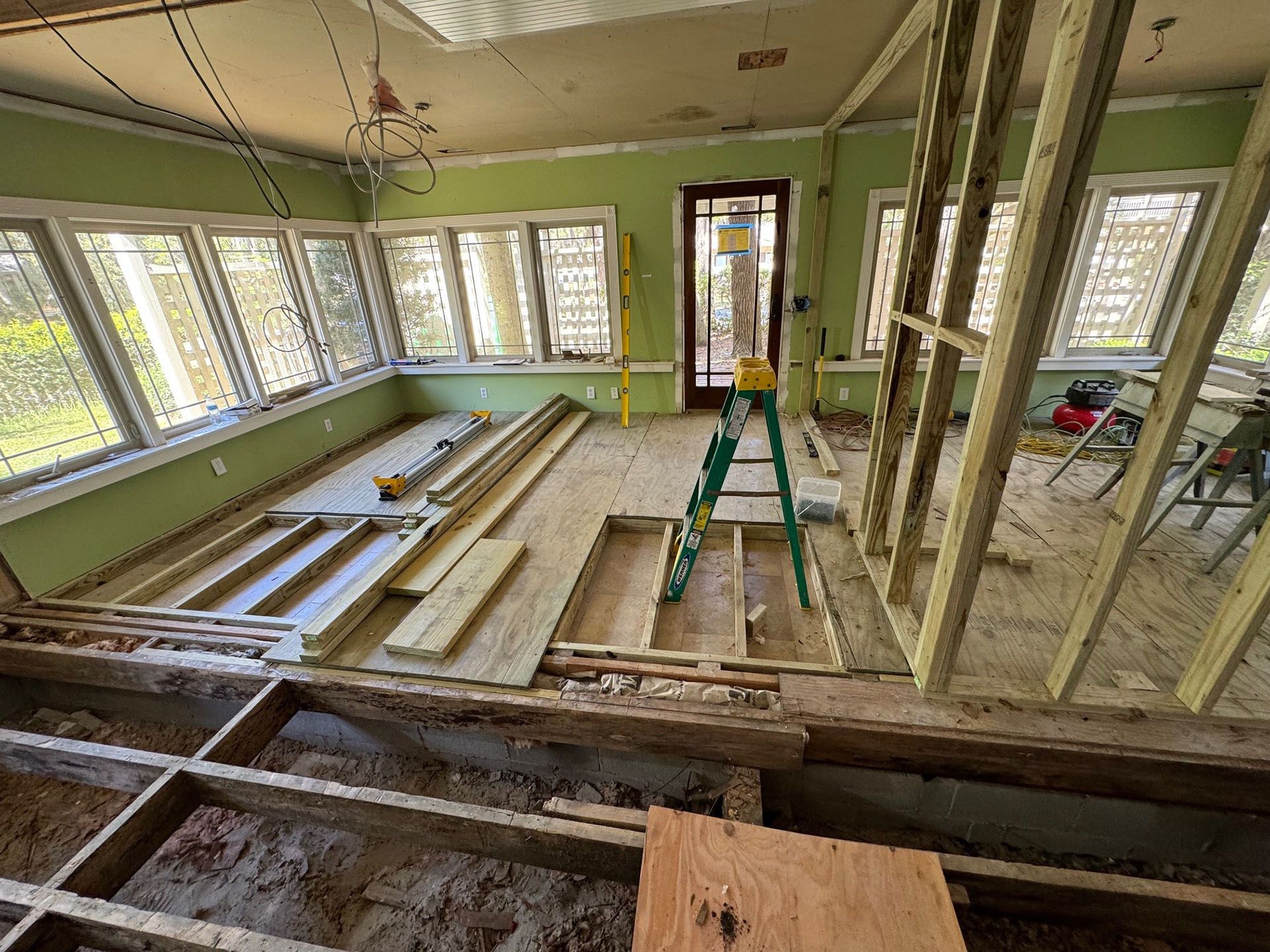 Termite Damage - Room under construction with exposed floor beams and wood framing. Green walls and windows, door in the background.