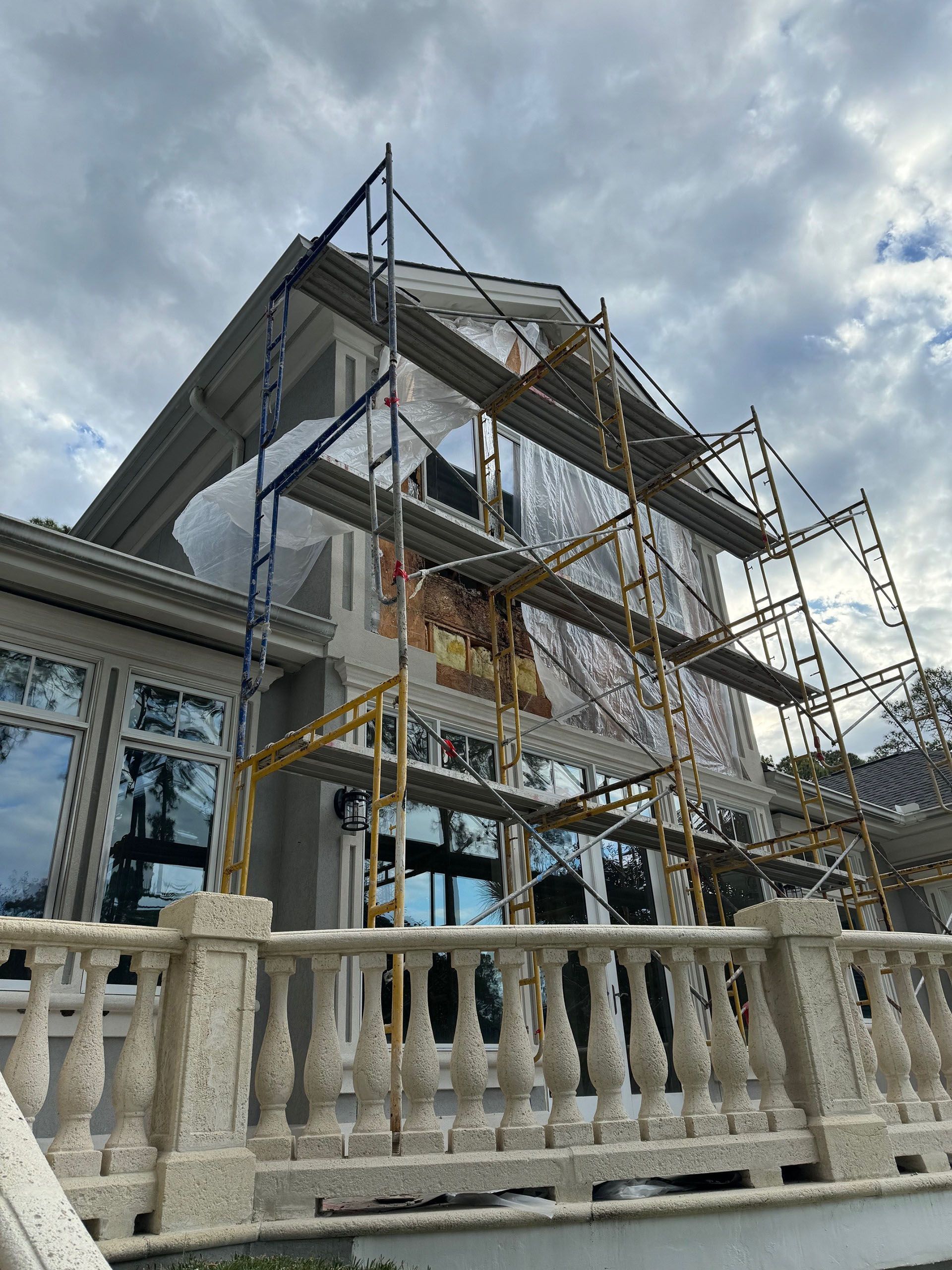 Termite Damage - House exterior under construction, scaffolding erected. Grey sky, white building with large windows and balcony.