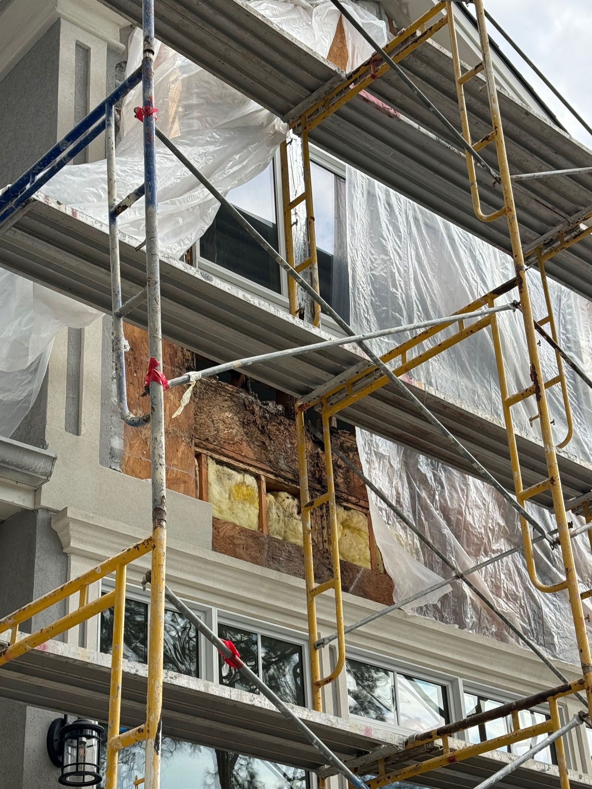 Termite Damage - Exterior house undergoing renovation with scaffolding, clear plastic covering damaged brick wall.