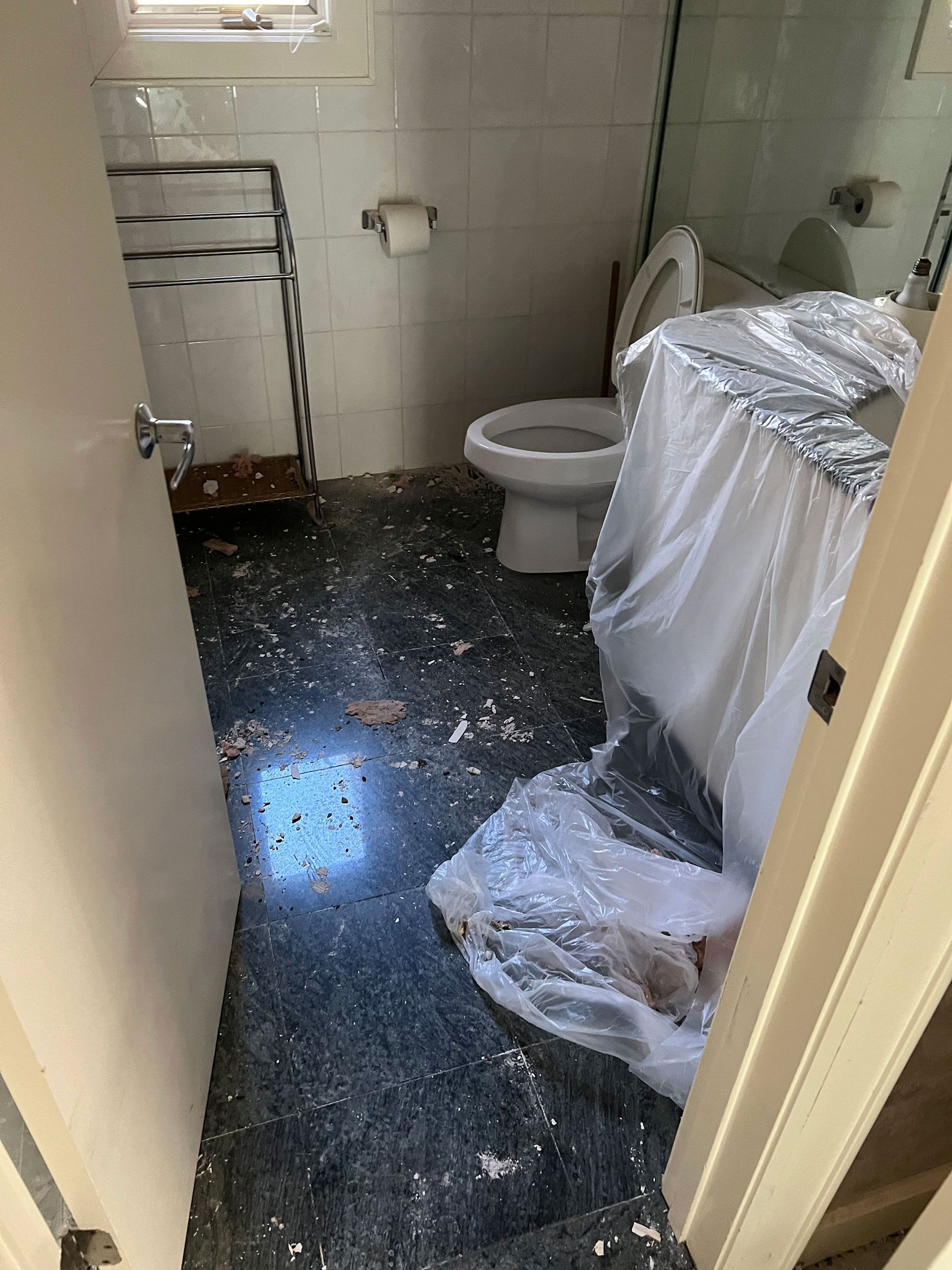 Bathroom with dark speckled floor, toilet, and plastic-covered counter. A towel rack is against a wall.