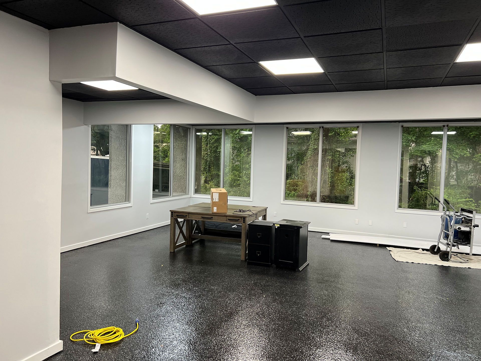 Carolina Rides - After: Interior of a room with a black epoxy floor, gray walls, large windows, and a black ceiling with square lights.