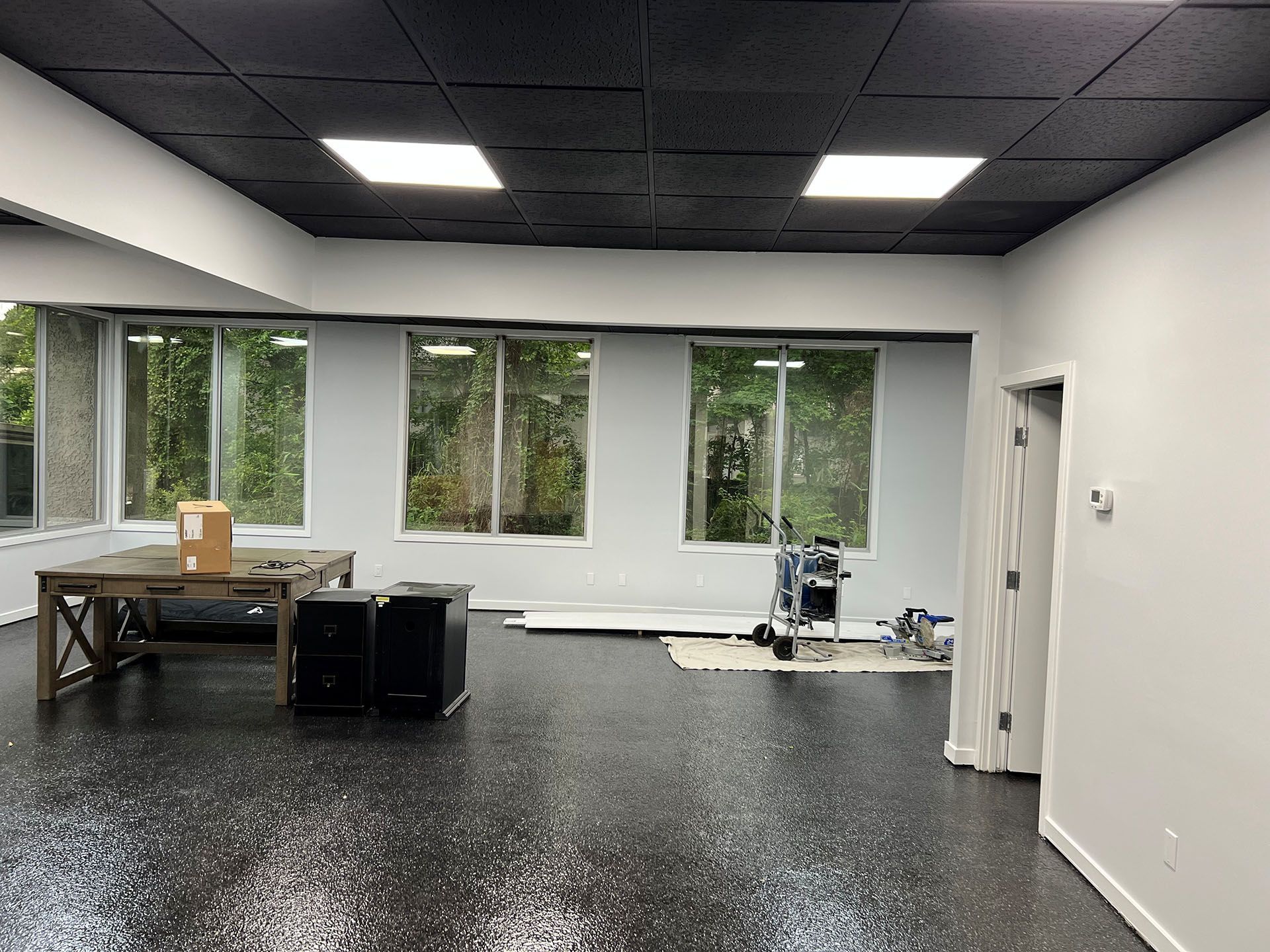 Carolina Rides - After: Empty room with a black speckled floor, windows, and black ceiling with recessed lights.